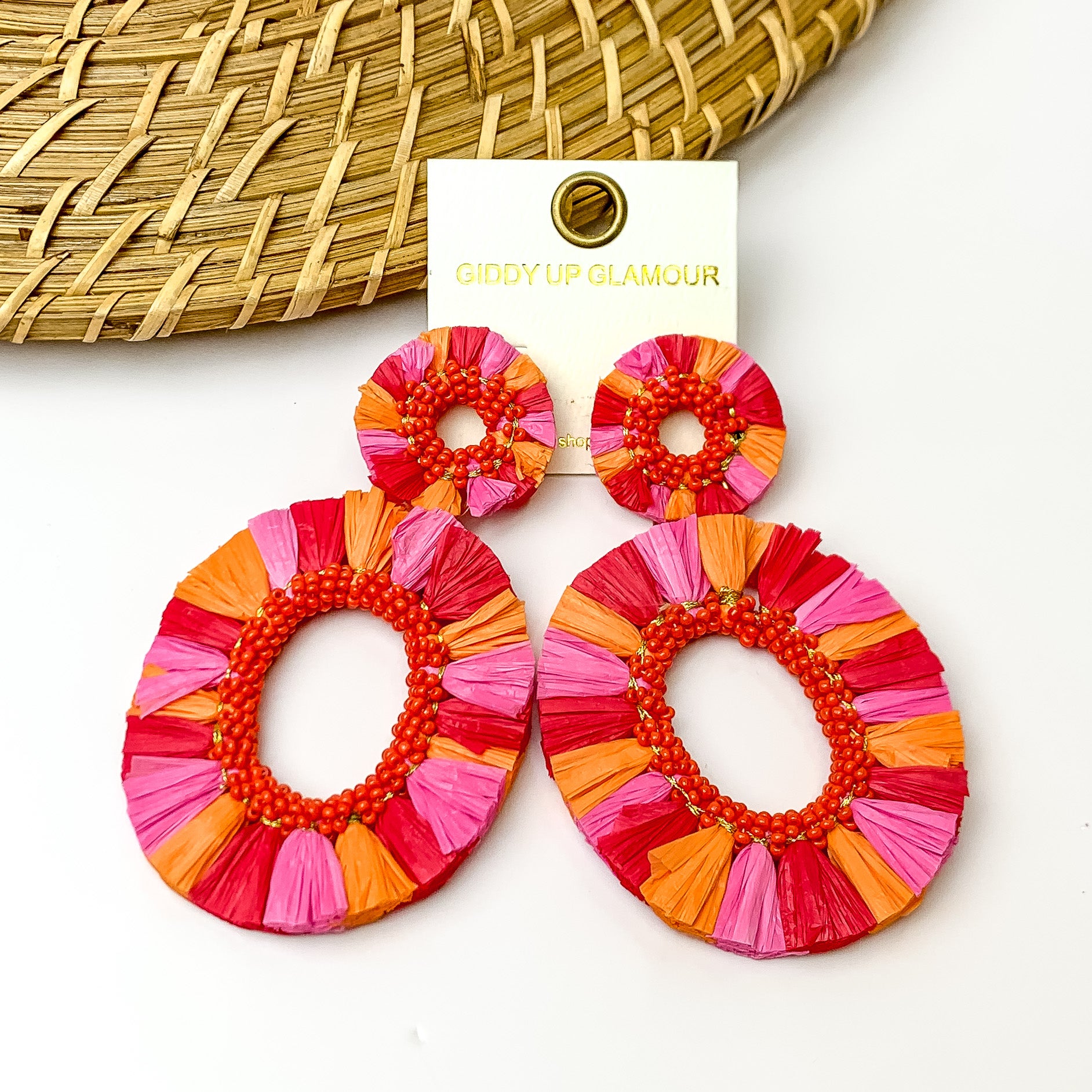 Red, pink, and orange fringe open hoops with orange beads on the inside. Pictured on a white background with a wood like decoration in the top left corner.