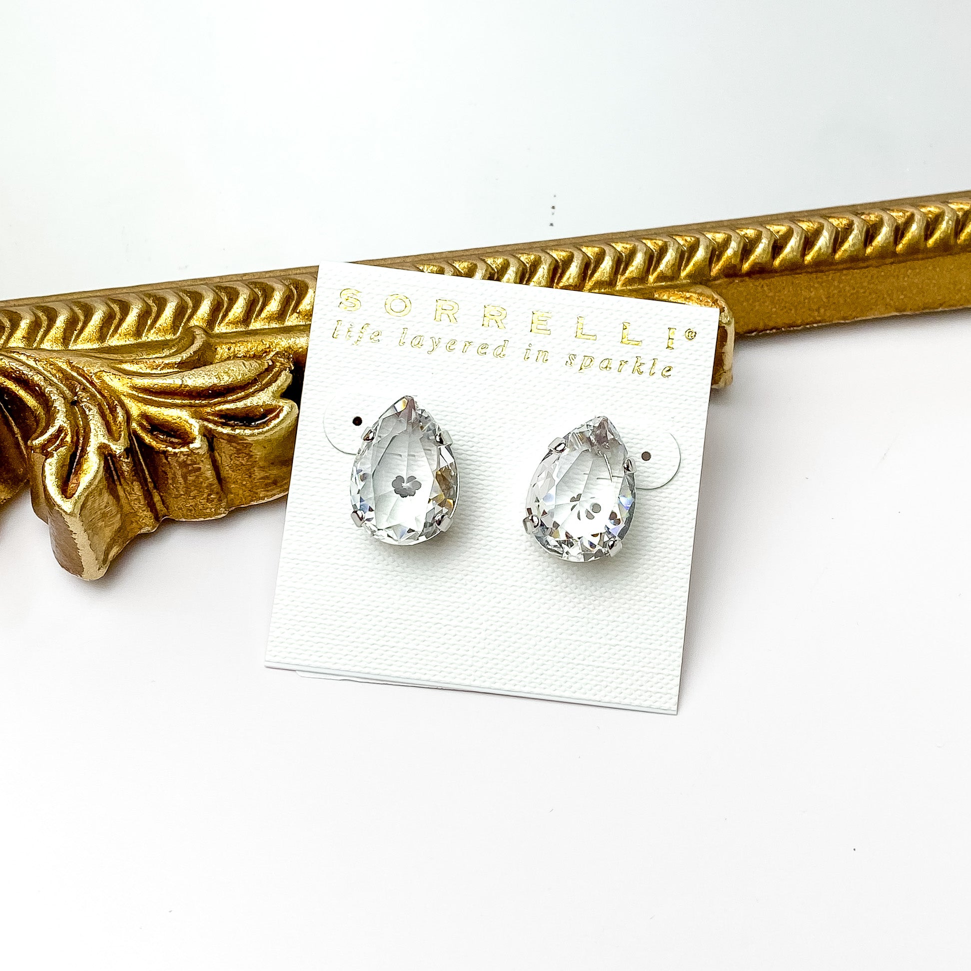 Single clear crystal stud earrings with a silver backing. Pictured on a white background with a gold figure through the middle