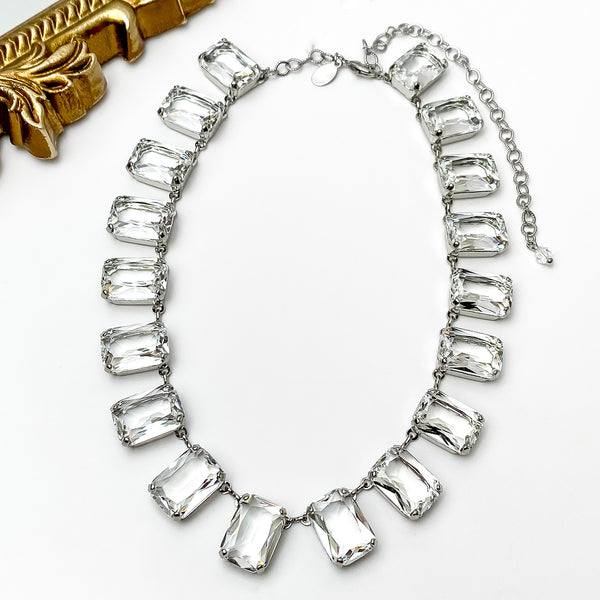 Clear rectangle crystal necklace. This necklace has a silver setting. This necklace is pictured on a white background with a gold mirror in the top left corner.   