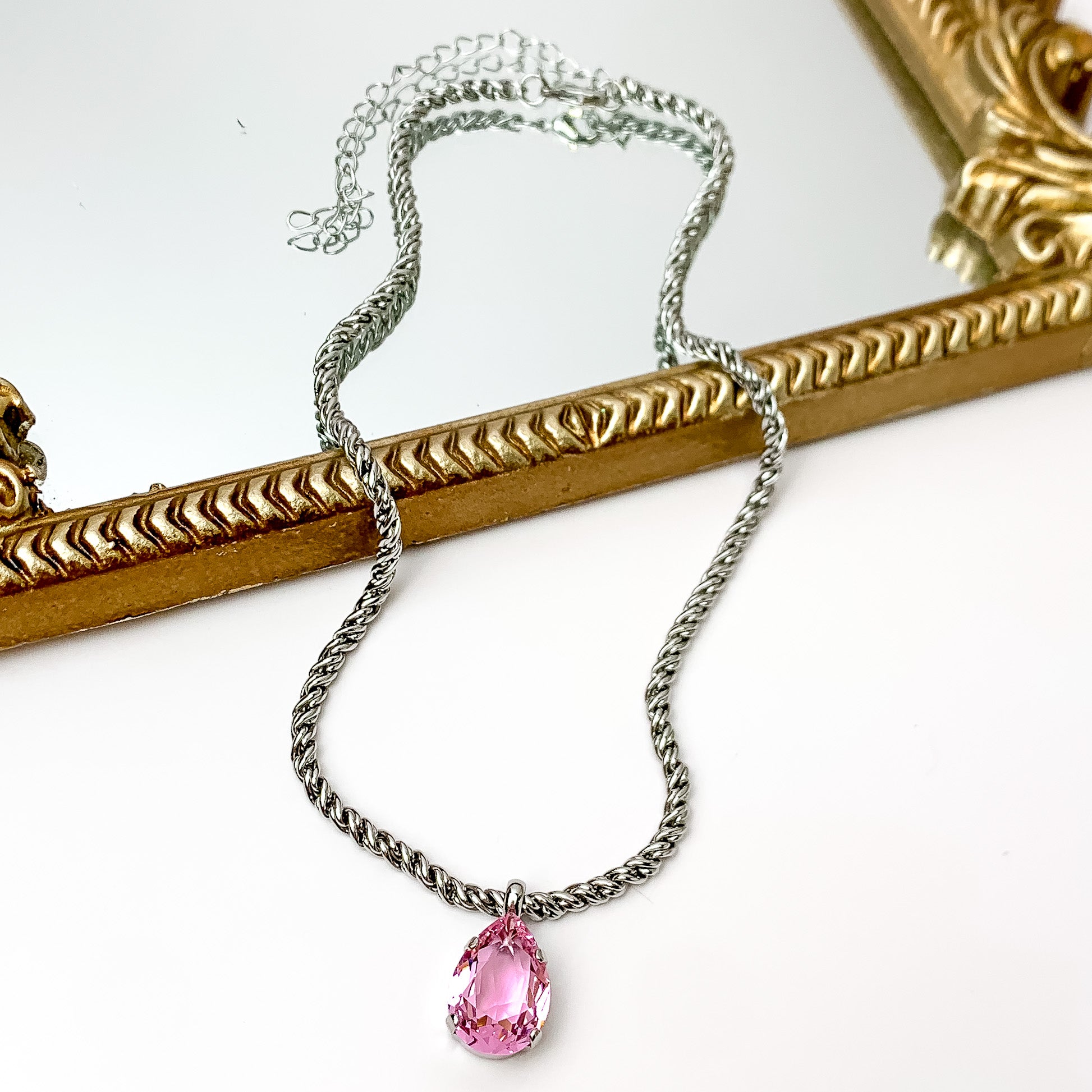 Silver necklace with light pink pendant at the end. Pictured on a white background with a mirror at the top.