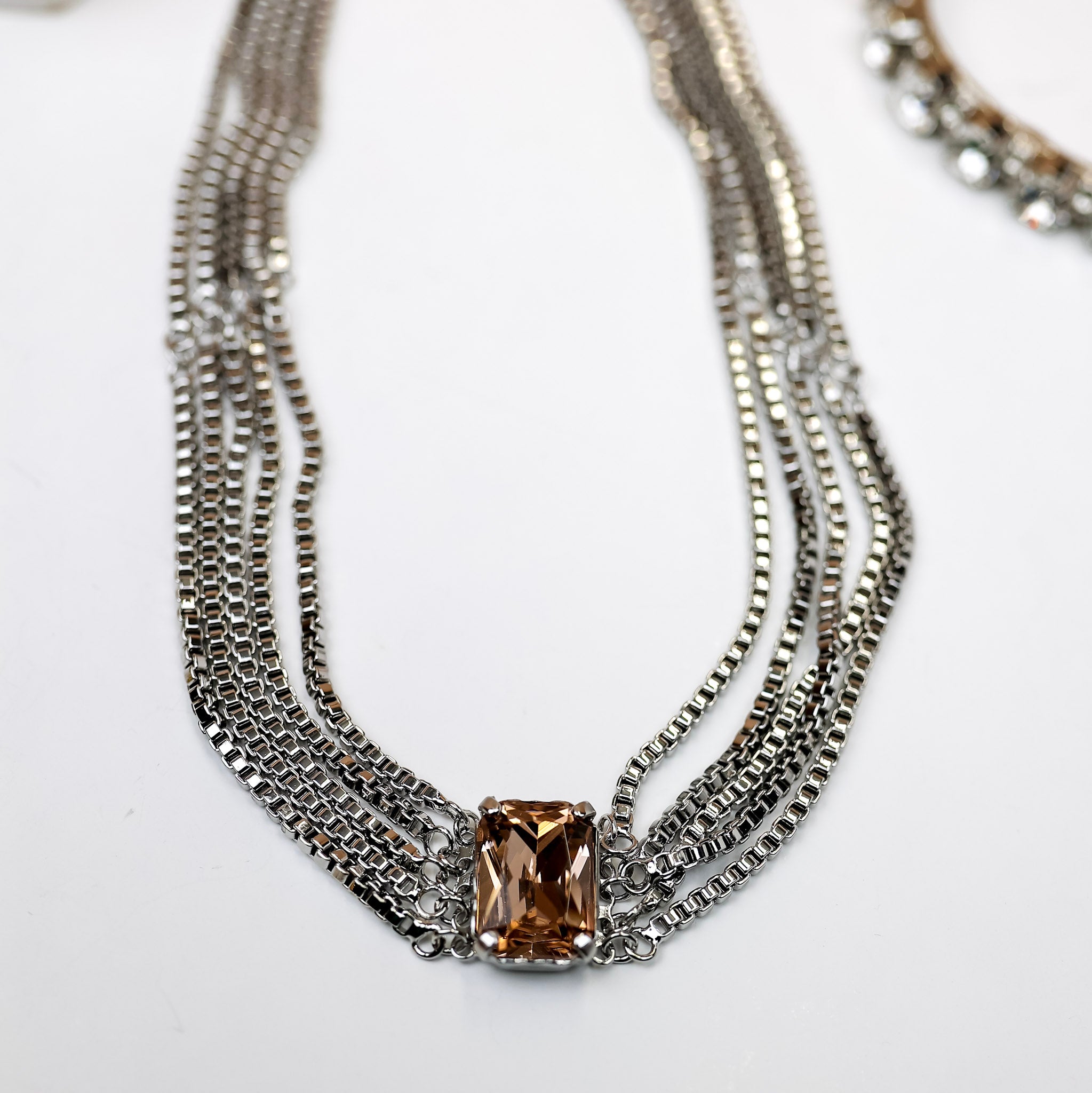 A silver-tone necklace with multiple box-chain strands that meet with a topaz emerald cut crystal.