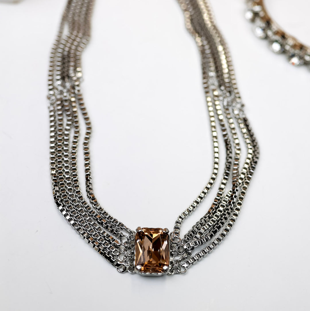 A silver-tone necklace with multiple box-chain strands that meet with a topaz emerald cut crystal.