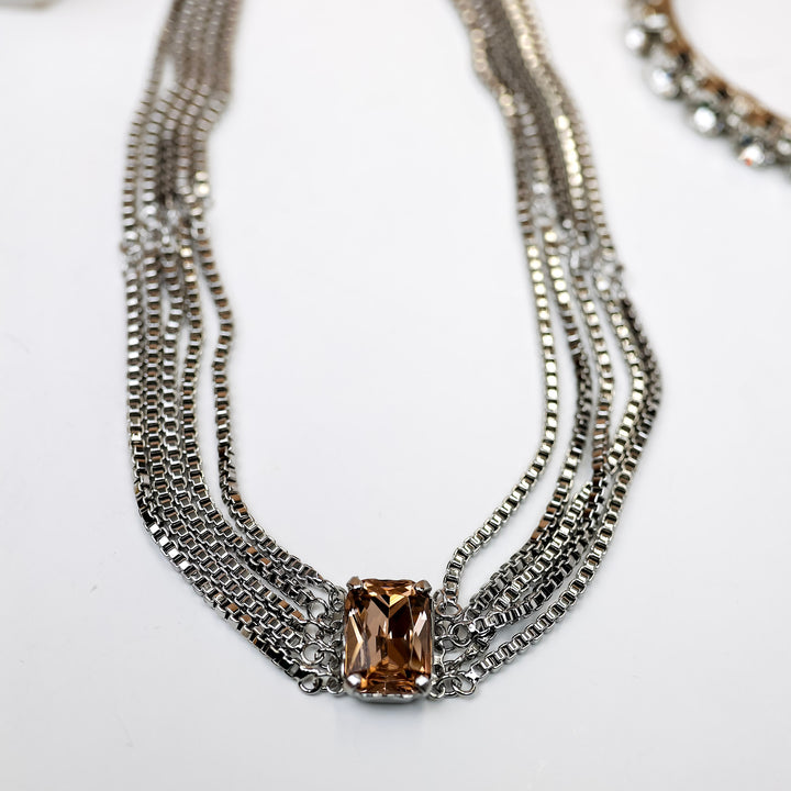 A silver-tone necklace with multiple box-chain strands that meet with a topaz emerald cut crystal.