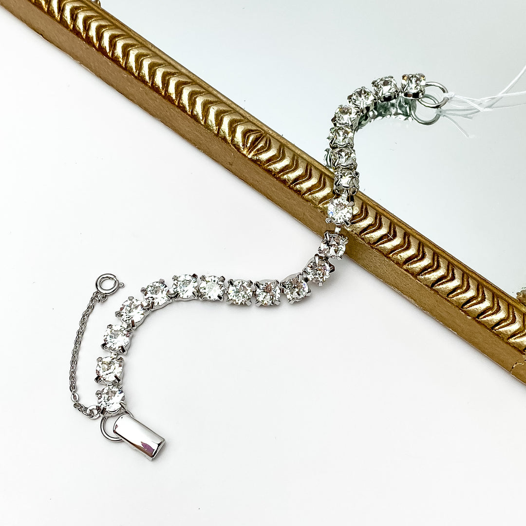 Silver Tennis bracelet with clear crystals wrapped around it. Pictured with a white background and a gold trim through the middle