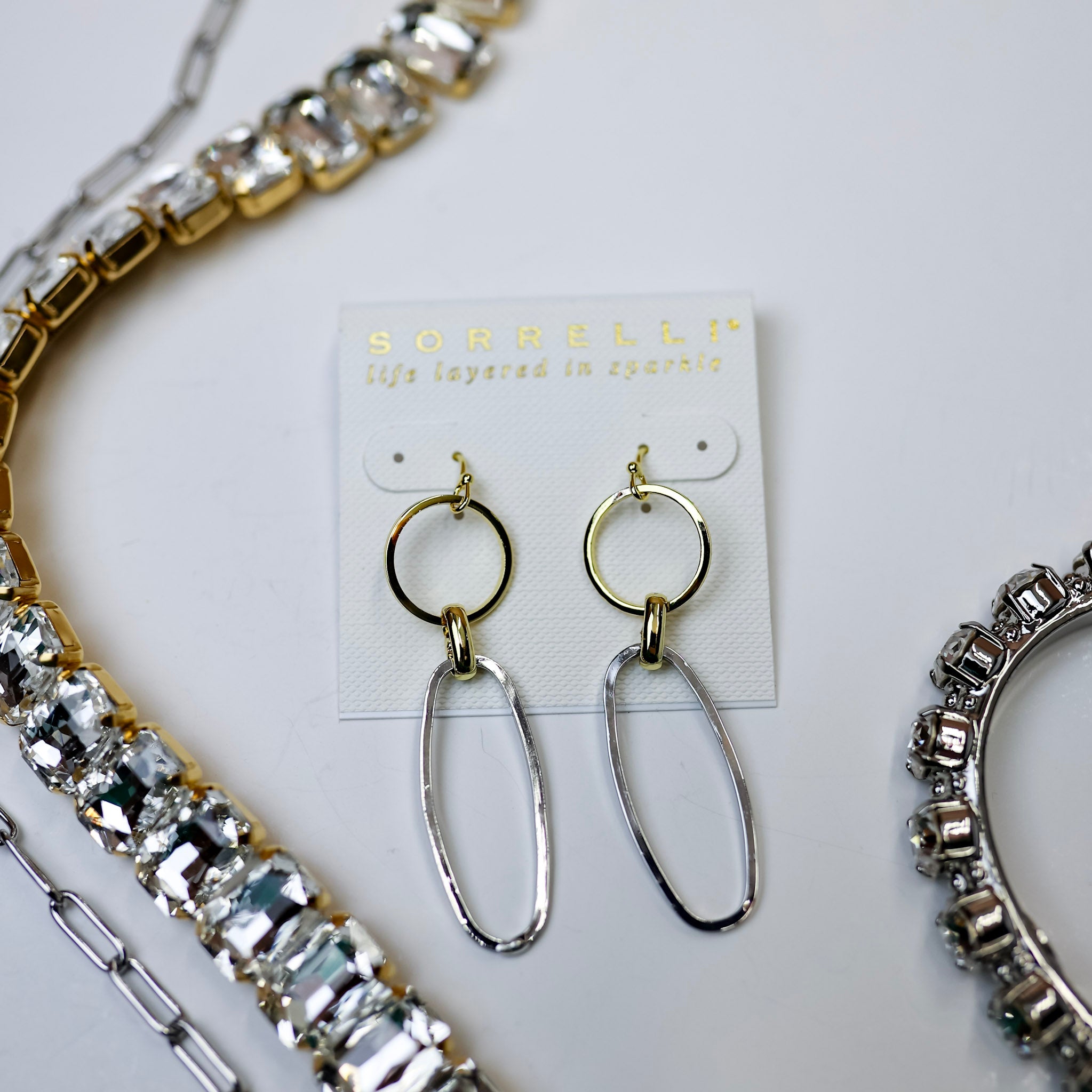 A pair of circle and oval dangle earrings that are a mix of silver and gold tone.