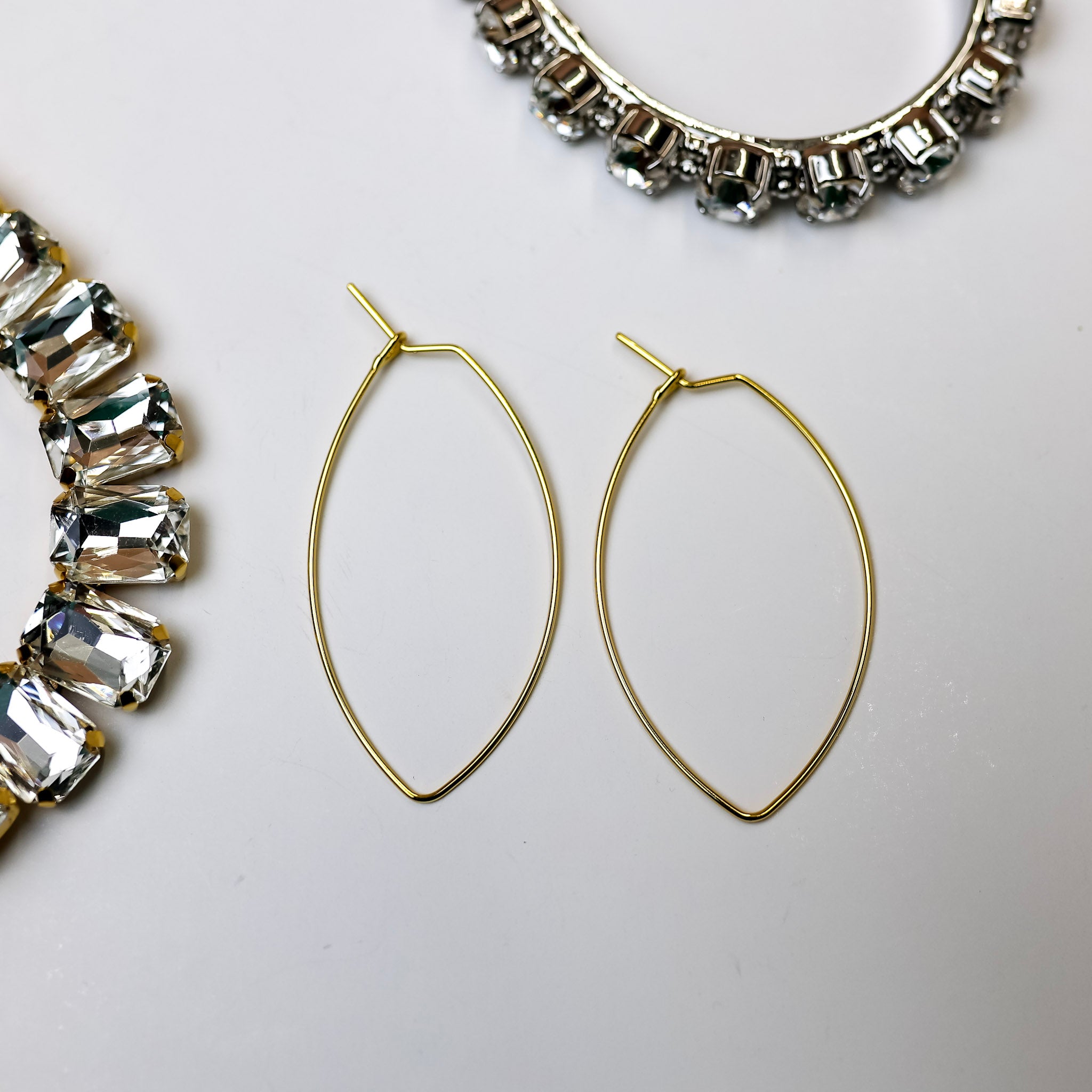 A pair of gold-tone hoop earrings that are cat-eye shape. Pictured on a gold background with crystal necklaces.