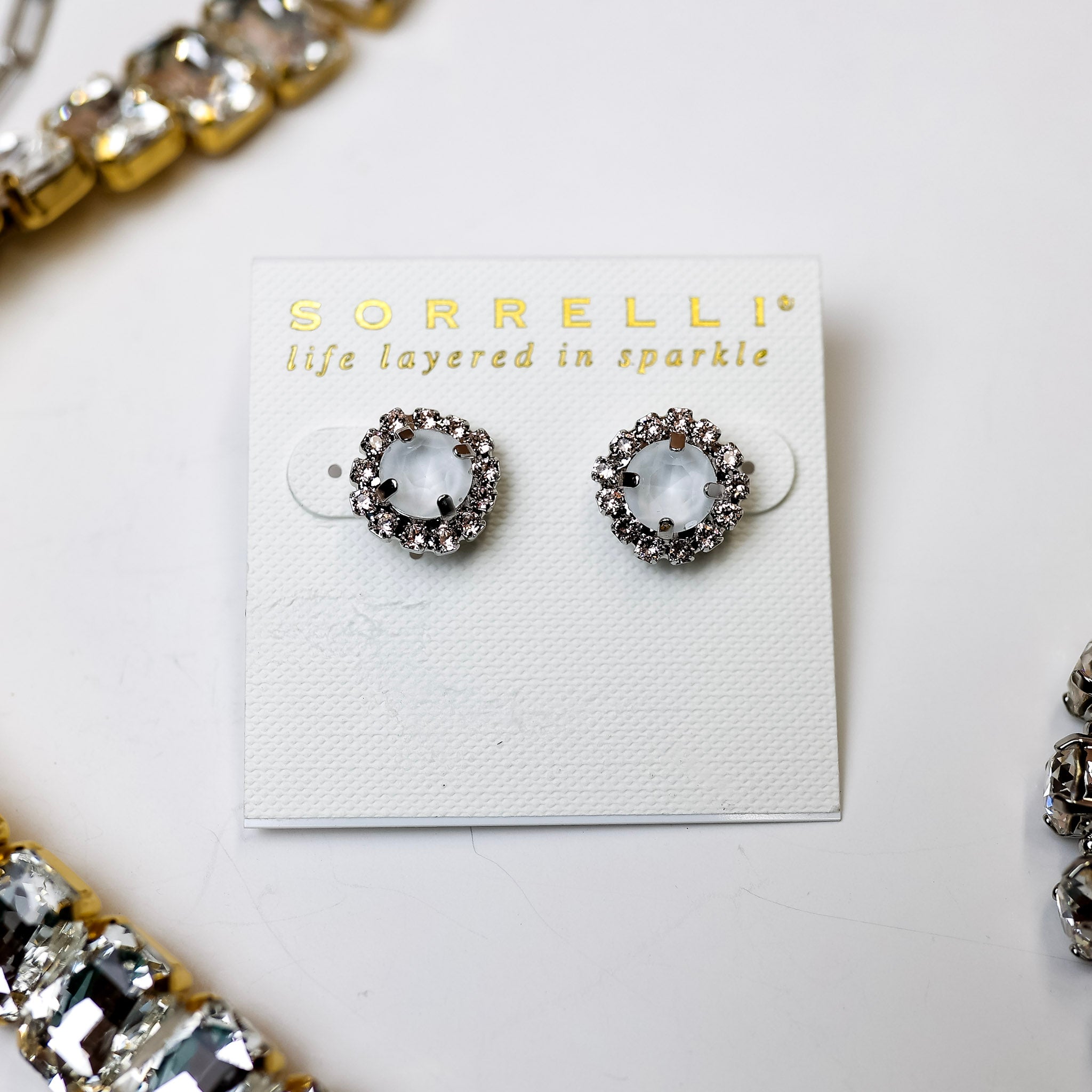 A pair of ivory circle crystal stud earrings with a clear crystal outline. Pictured on a white background with crystal necklaces.