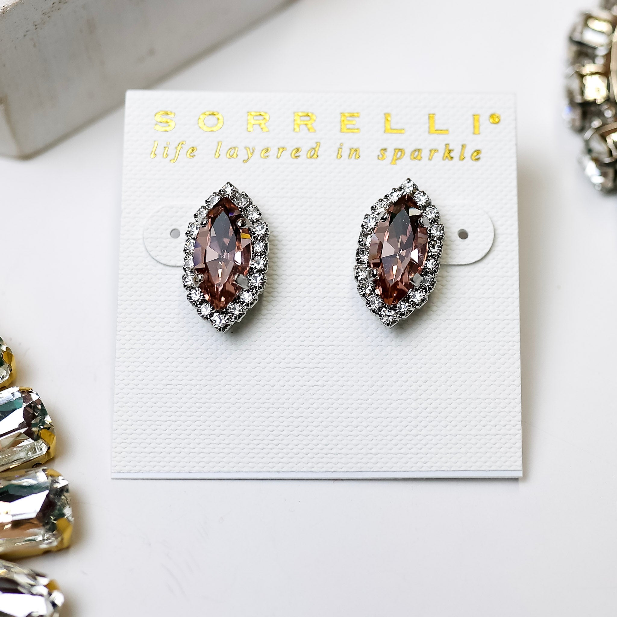 A pair of cat-eye shape crystal studs that are a dark rose color. The earrings have a clear crystal outline.