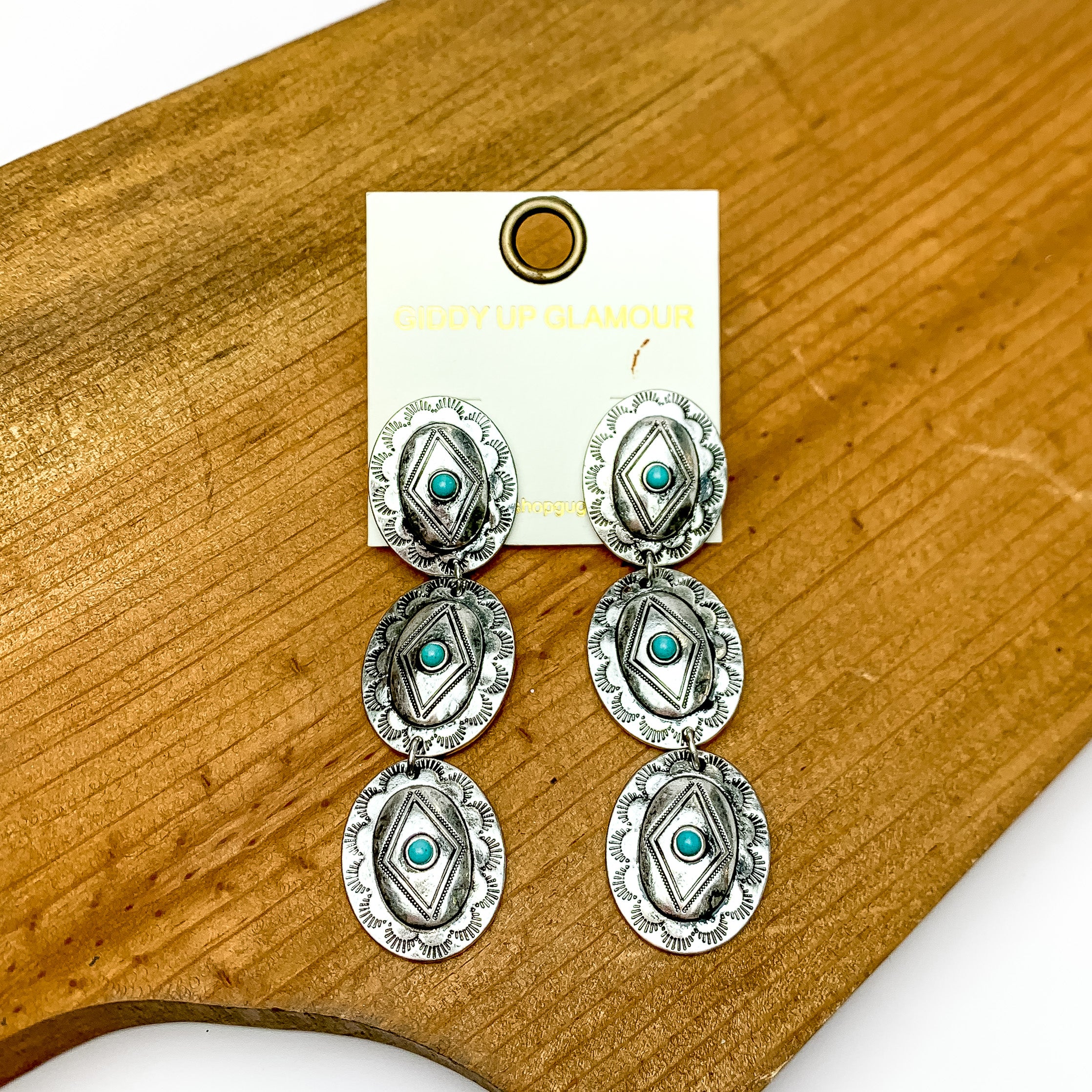 Three tier silver tone and turquois oval shape dangle earrings. Pictured on a wood piece with white in the back.