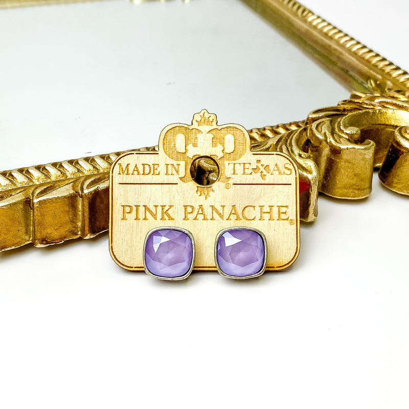 Lilac purple cushion cut crystal stud earrings with a silver setting. These earrings are pictured on a Pink Panache wood holder in front of a gold mirror and on a white background.