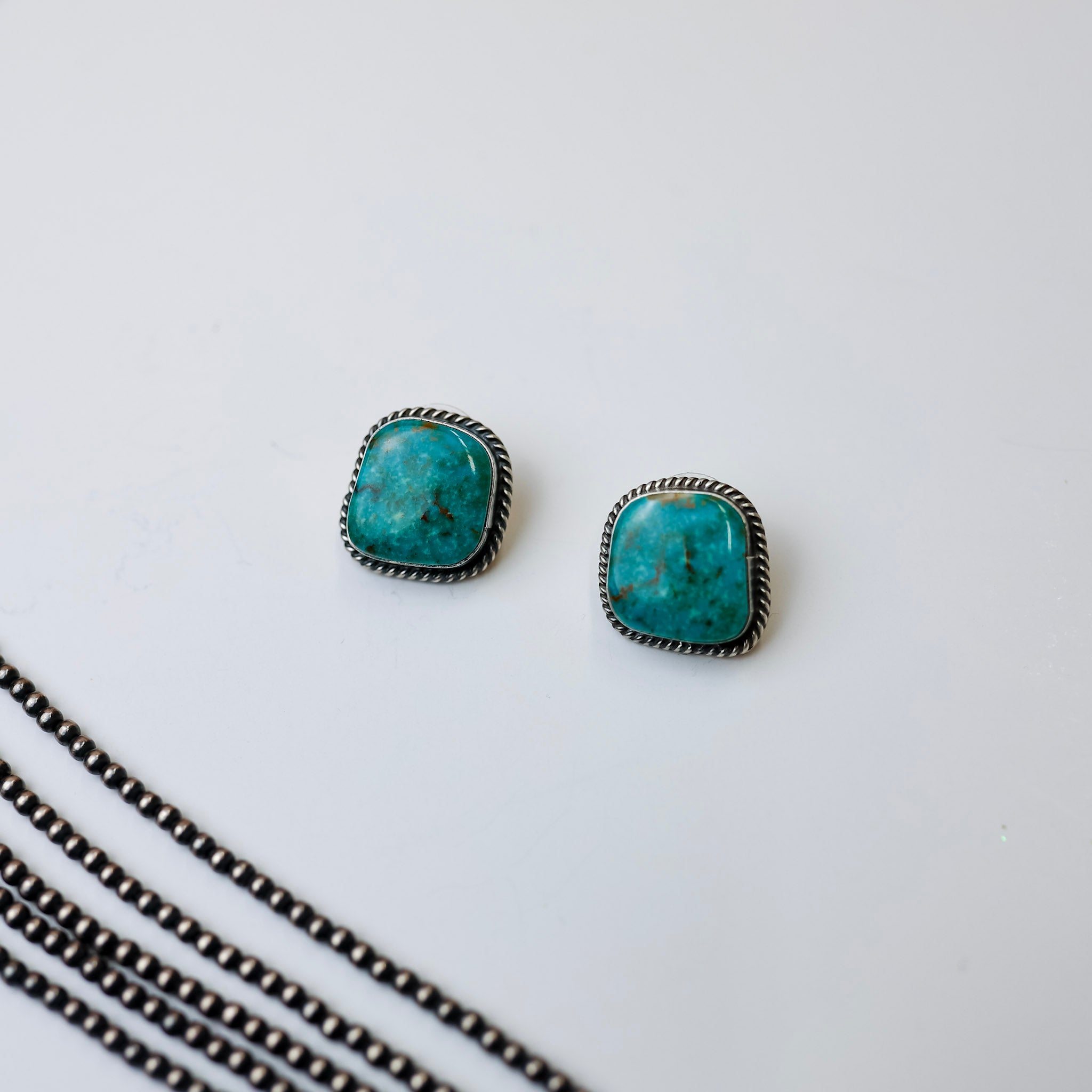 Elouise Kee Genuine Navajo Handmade Sterling Silver Indian Handcrafted Kingman turquoise stud earrings. Background is white with navajo pearl necklaces in the bottom left corner. 