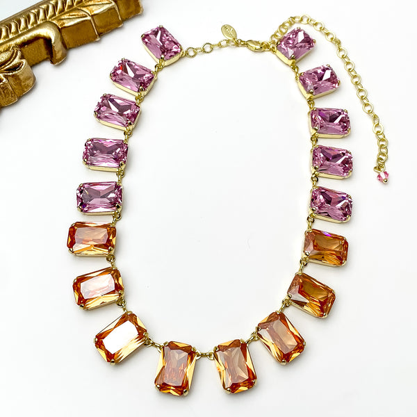 Pink and orange rectangle crystal necklace. This necklace has a gold setting. This necklace is pictured on a white background with a gold mirror in the top left corner.   