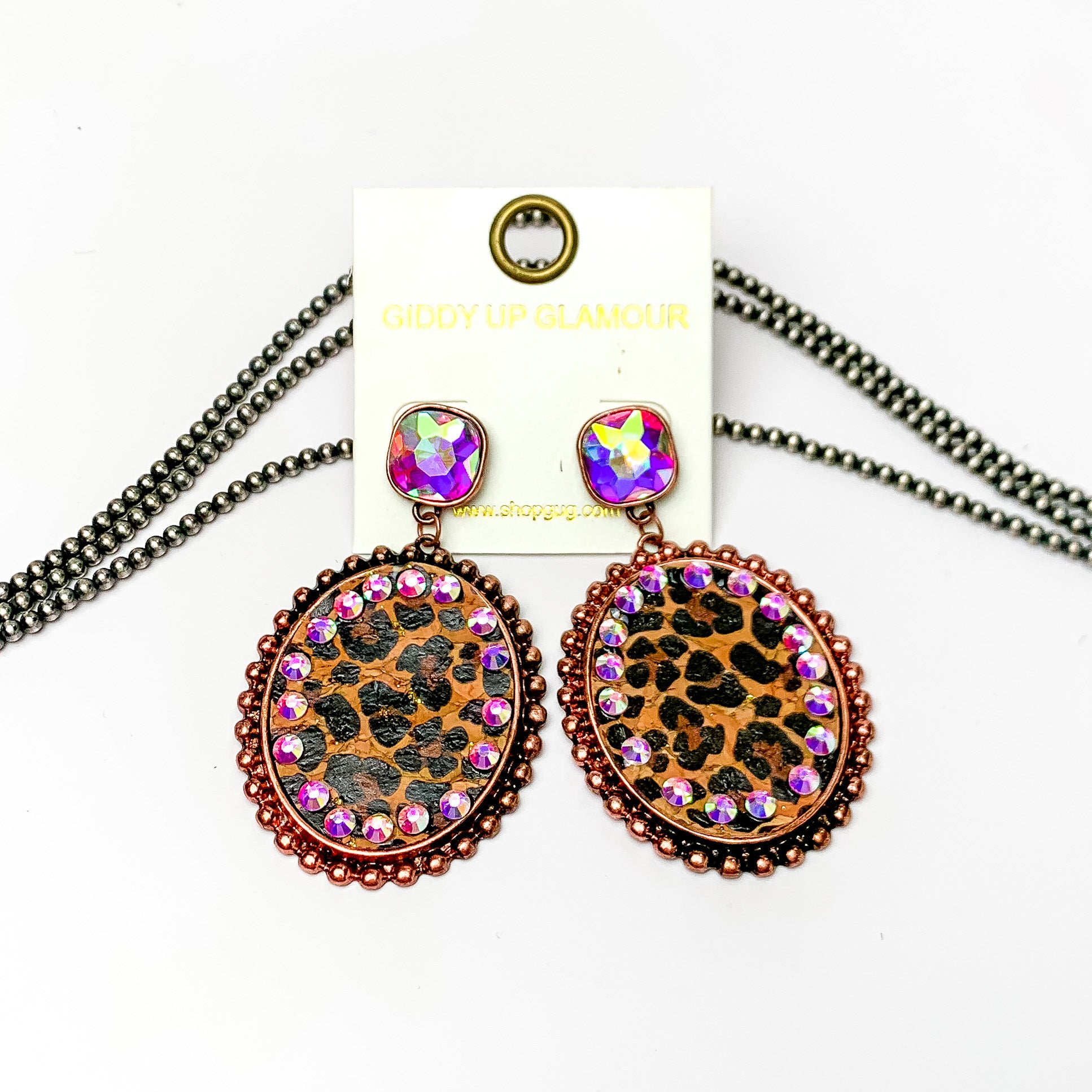 These earrings are oval shaped with leopard print inlay with the outline of the earing is copper but also has ab crystal going around the oval shape. These pair of earrings also have a ab crystal post style earring. Pictured on a white background with navajo pearls behind it.
