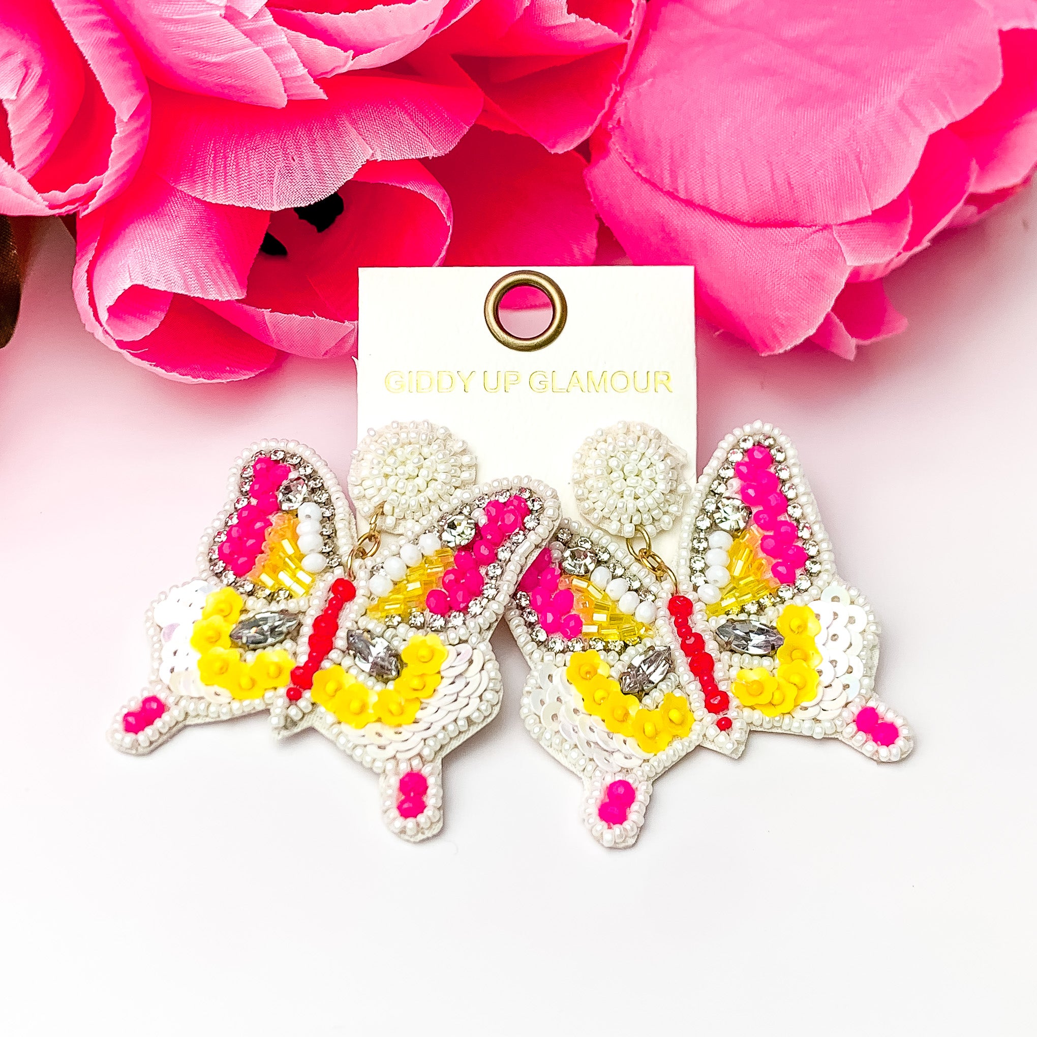 White pink and yellow beaded butterfly earrings. Pictured with a white background and pink roses at the top