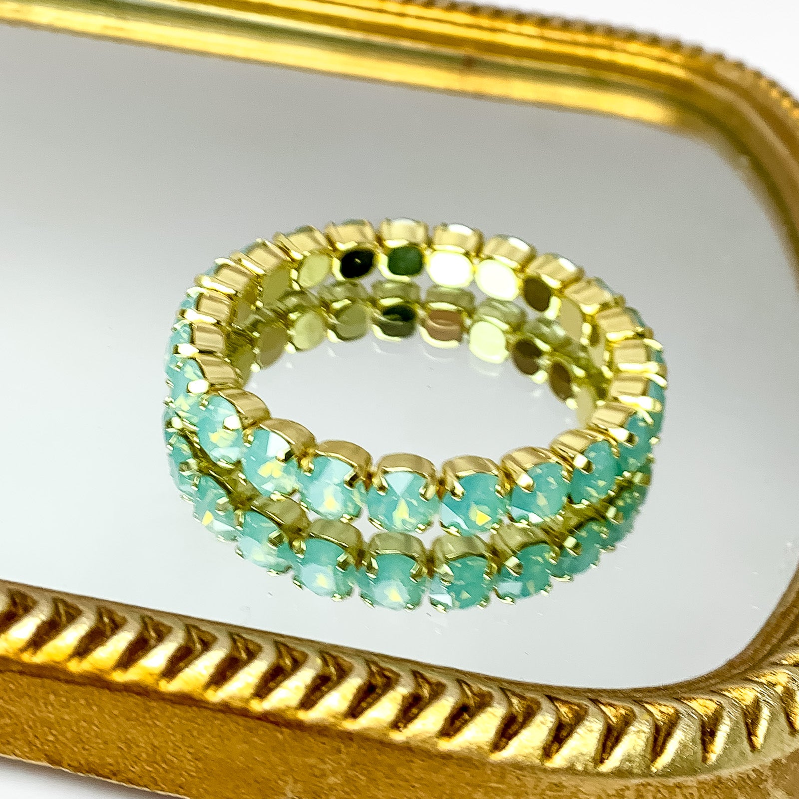 Stretchy light blue crystal bracelet with gold undertones. Pictured on a mirror with a gold trim.  