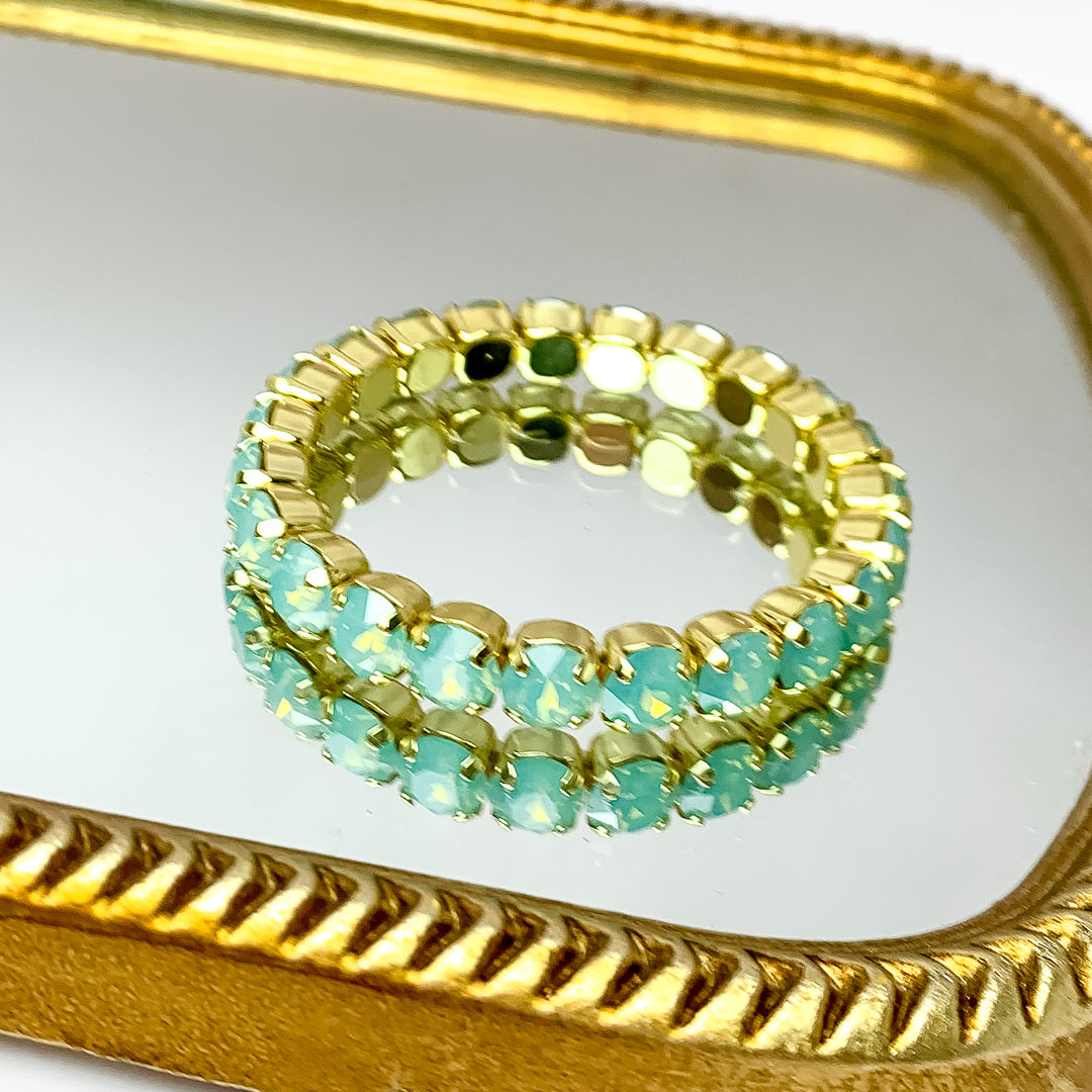 Stretchy light blue crystal bracelet with gold undertones. Pictured on a mirror with a gold trim.  