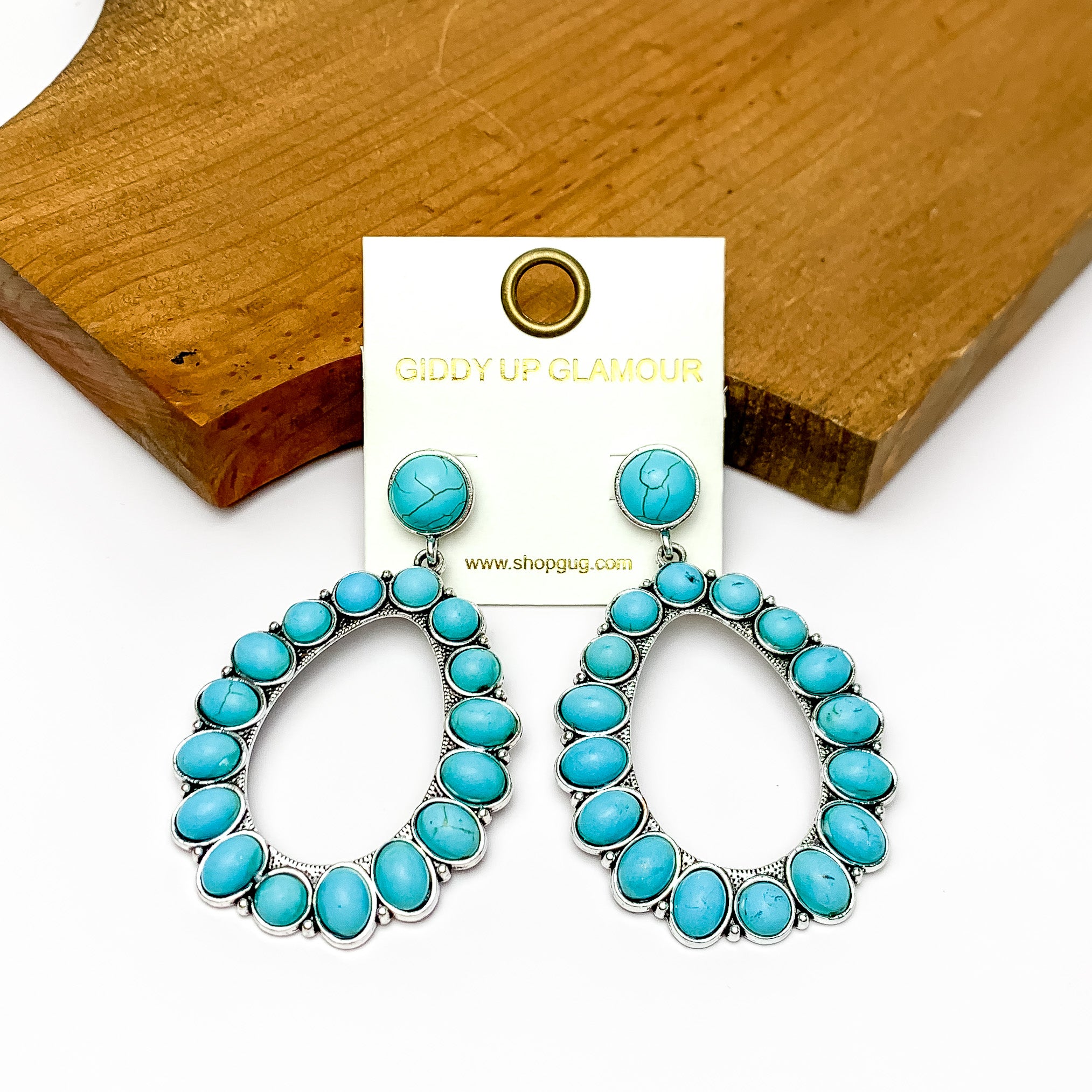 Large turquoise open droop hoops. Pictured on a white background with wood in the top corner. 