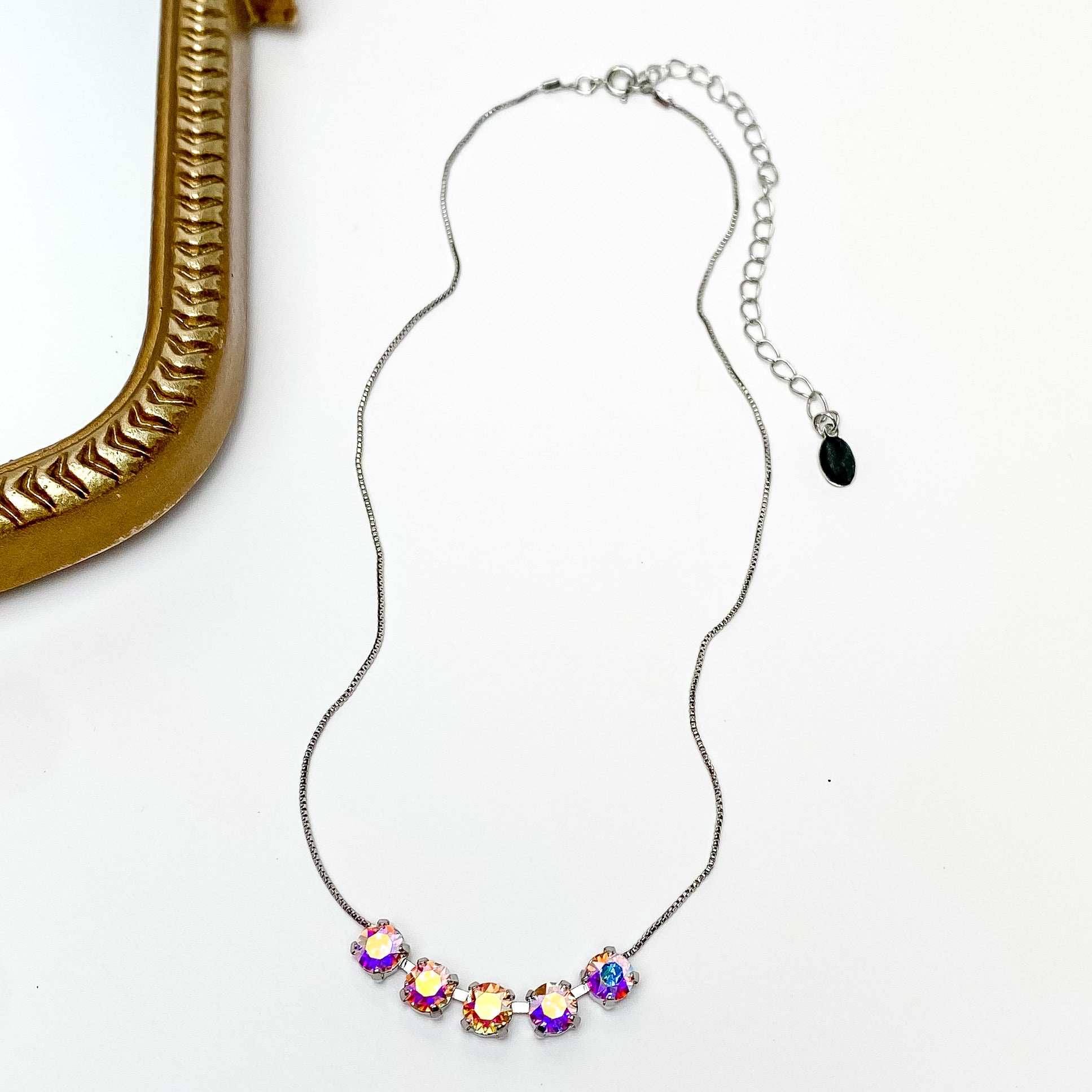 Pictured is a silver necklace with a five ab crystals. This necklace is pictured on a white background with a gold mirror on the left side.