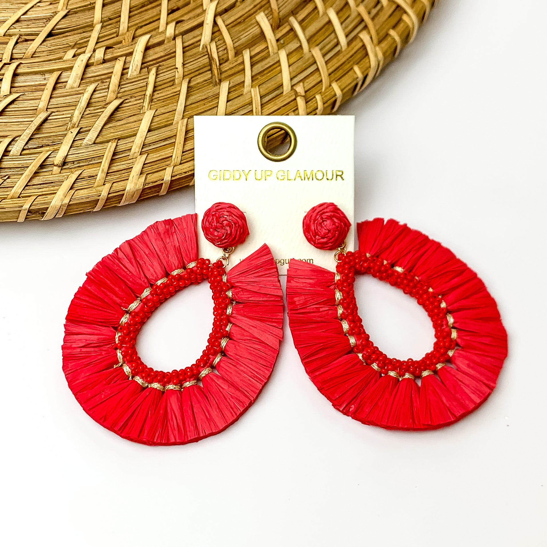 Red fringe open drop hoops with beads on the inside. Pictured on a white background with a wood like decoration in the top left