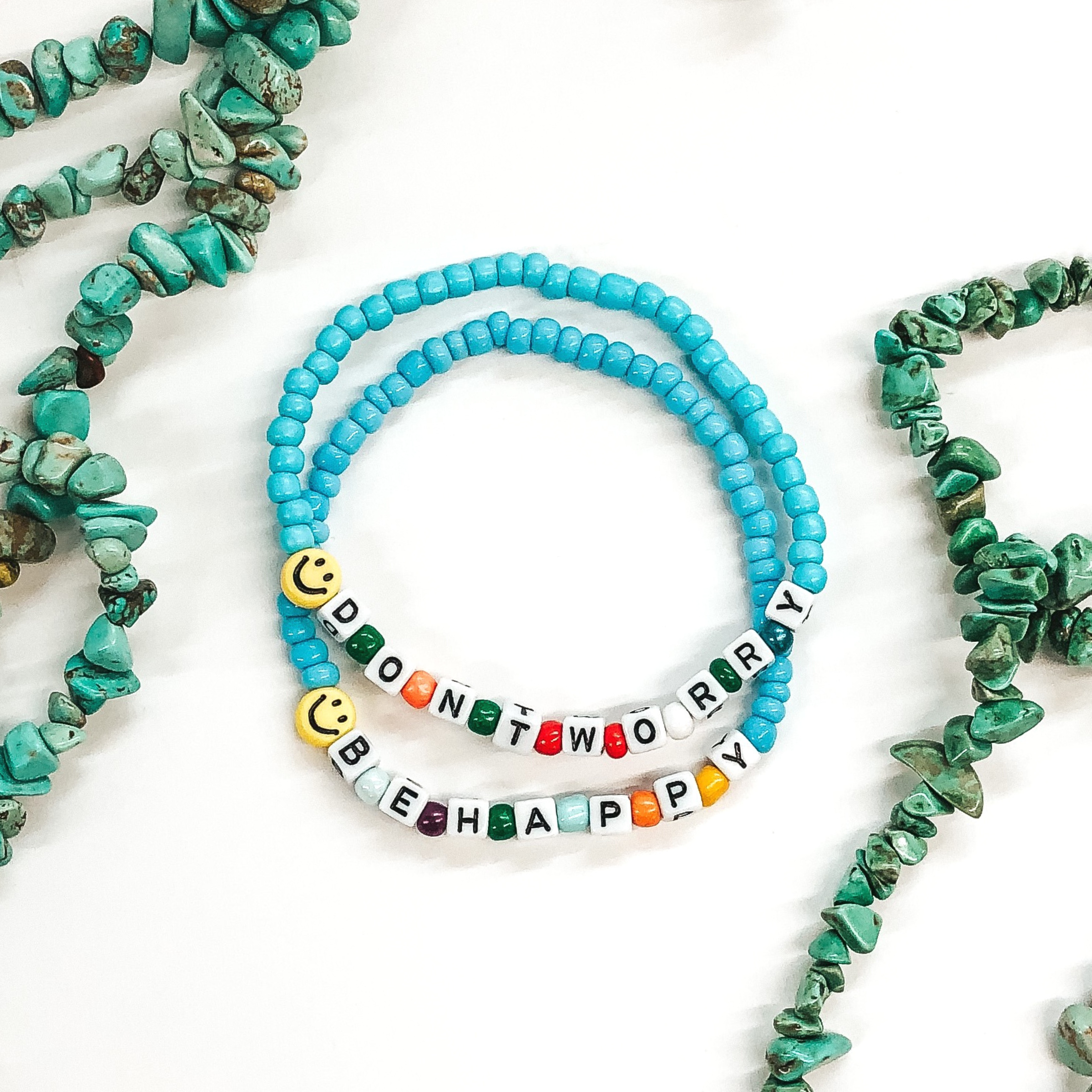 two light blue beaded bracelets with smiley face beads and lettering that say dont worry be happy 