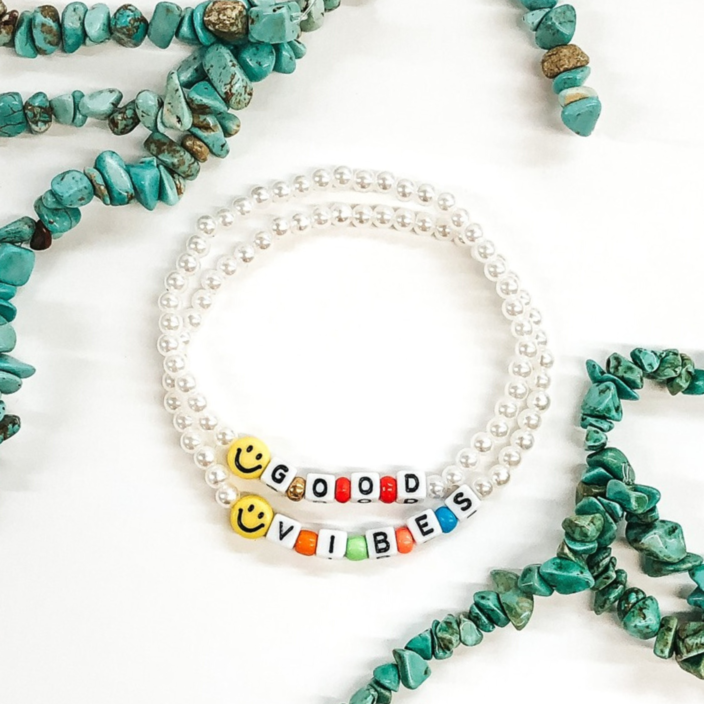 two white beaded bracelets with smiley face beads and lettering that says good vibes