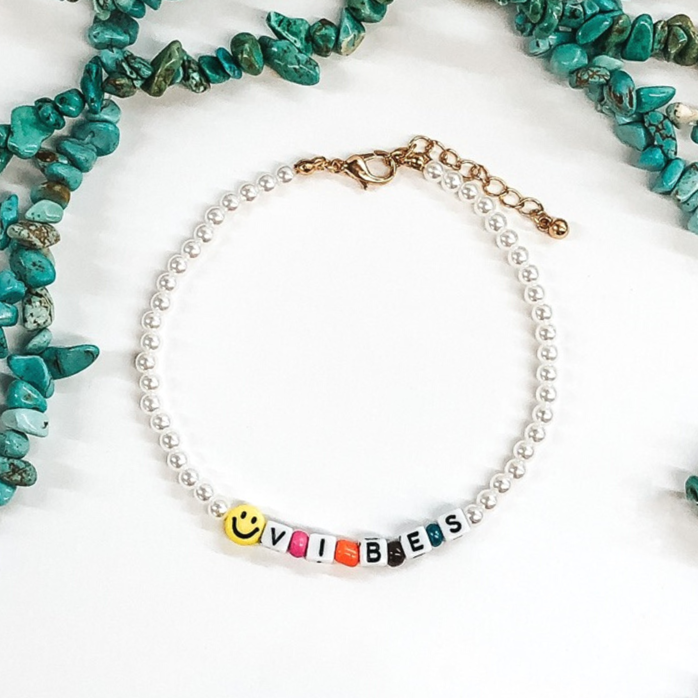 white beaded adjustable anklet with letter beads that say vibes and a smiley face bead