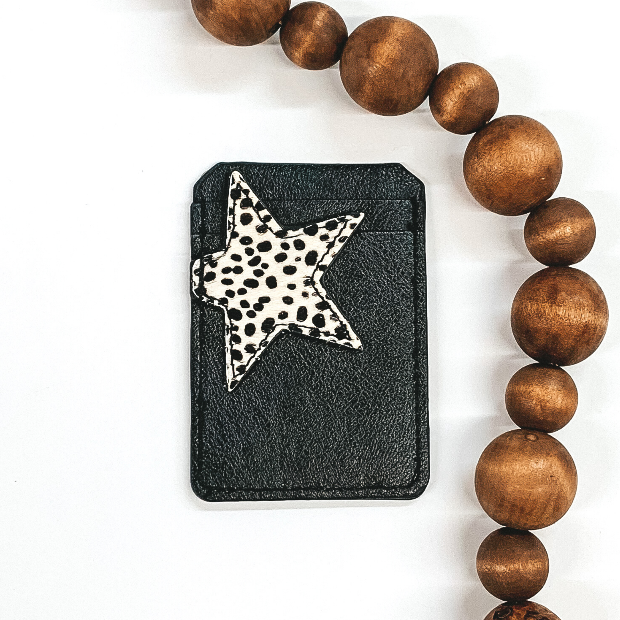 Black card holder with two pockets that has a white star with black dots on the star on the front and can stick to the back of phones/phone cases