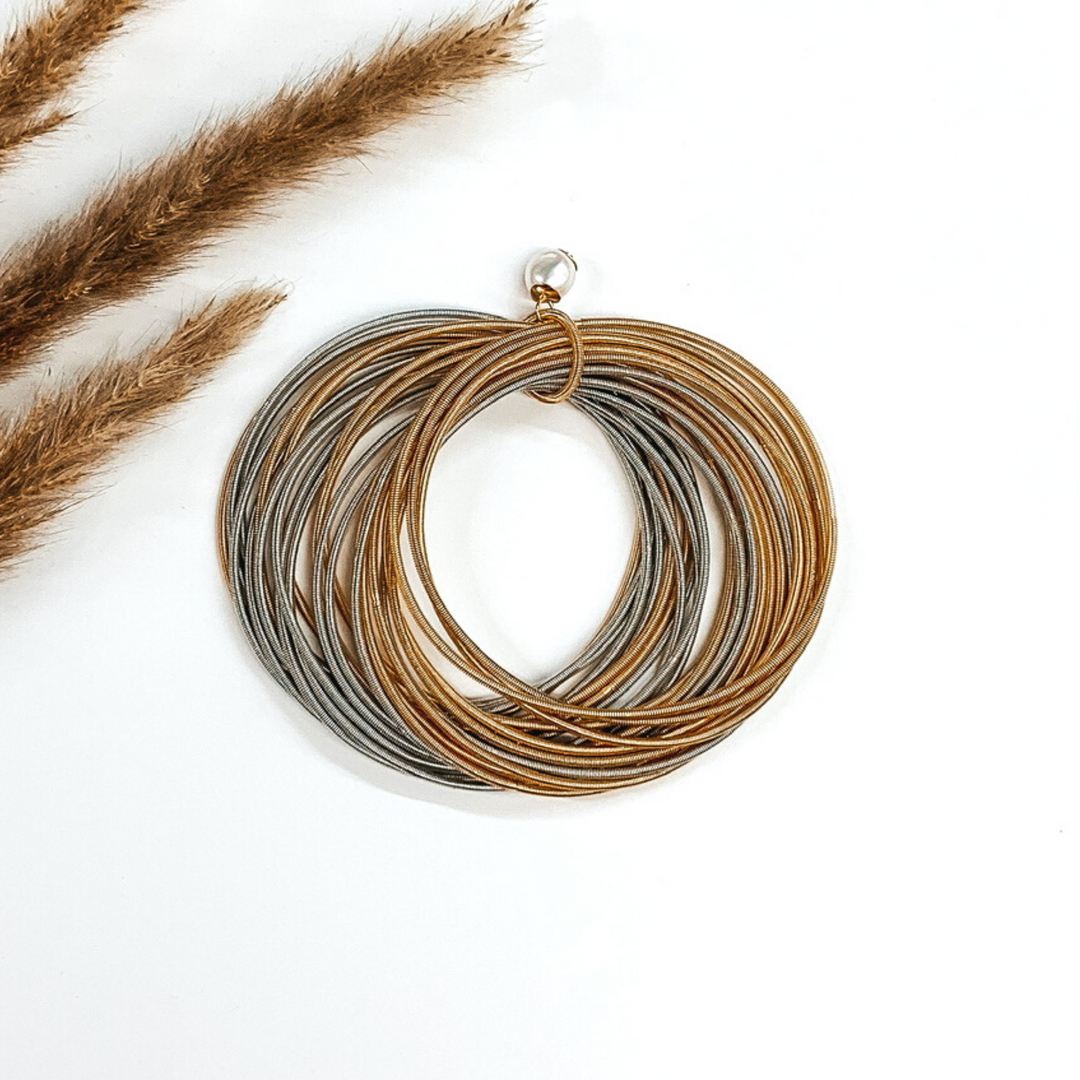 Thin gold and silver bracelets bunched together with a pearl beaded charm on a white background