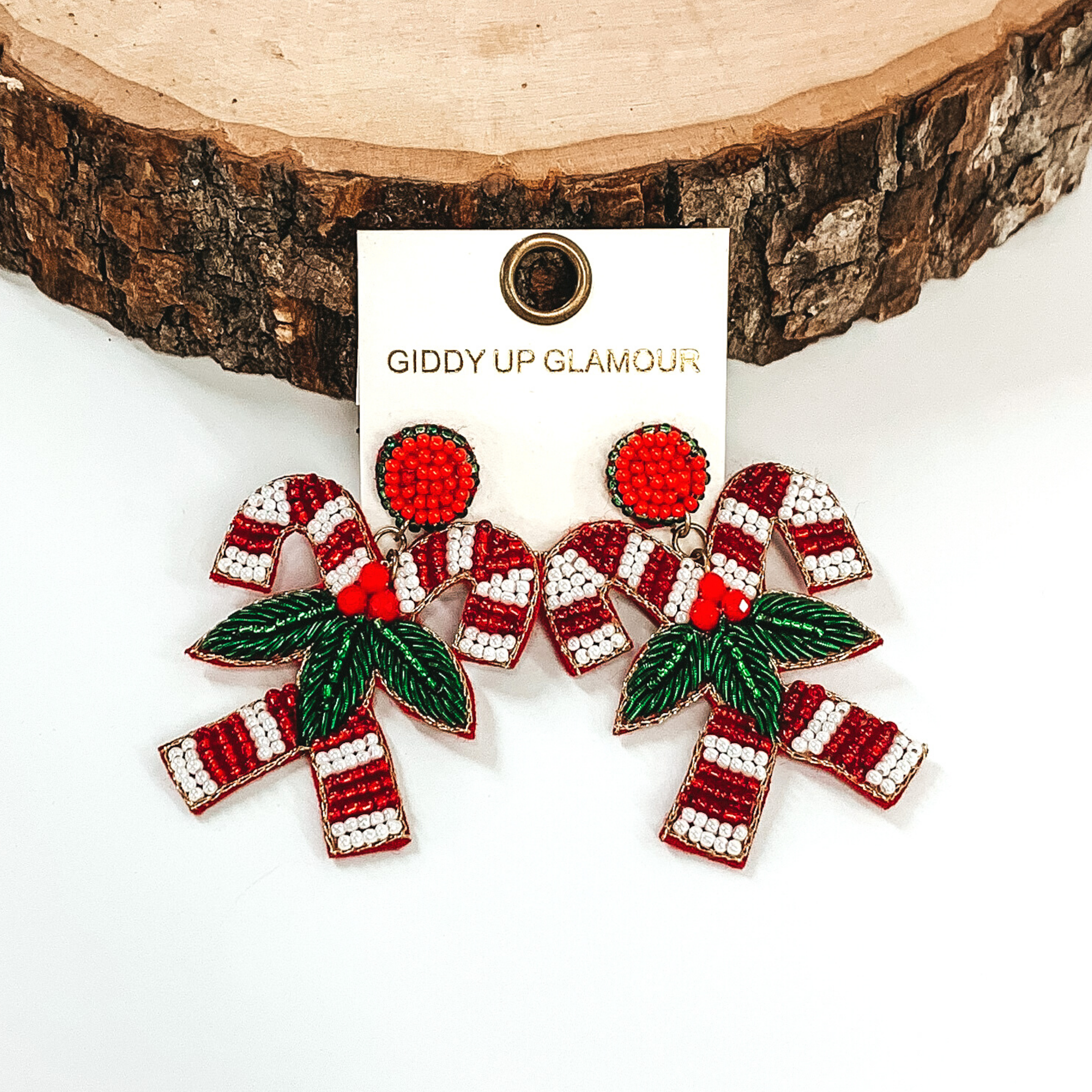 Red and white striped beaded candy canes earrings with them connected together with mistletoe on a white background. 
