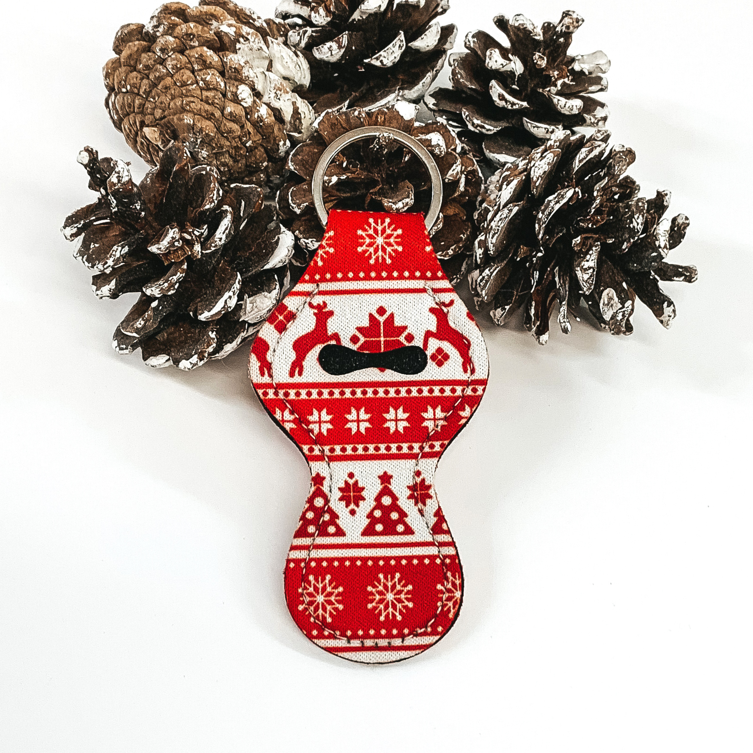 White lip balm holder with a red christmas print on a key ring. This lip balm holder is pictured on a white background with pine cones. 