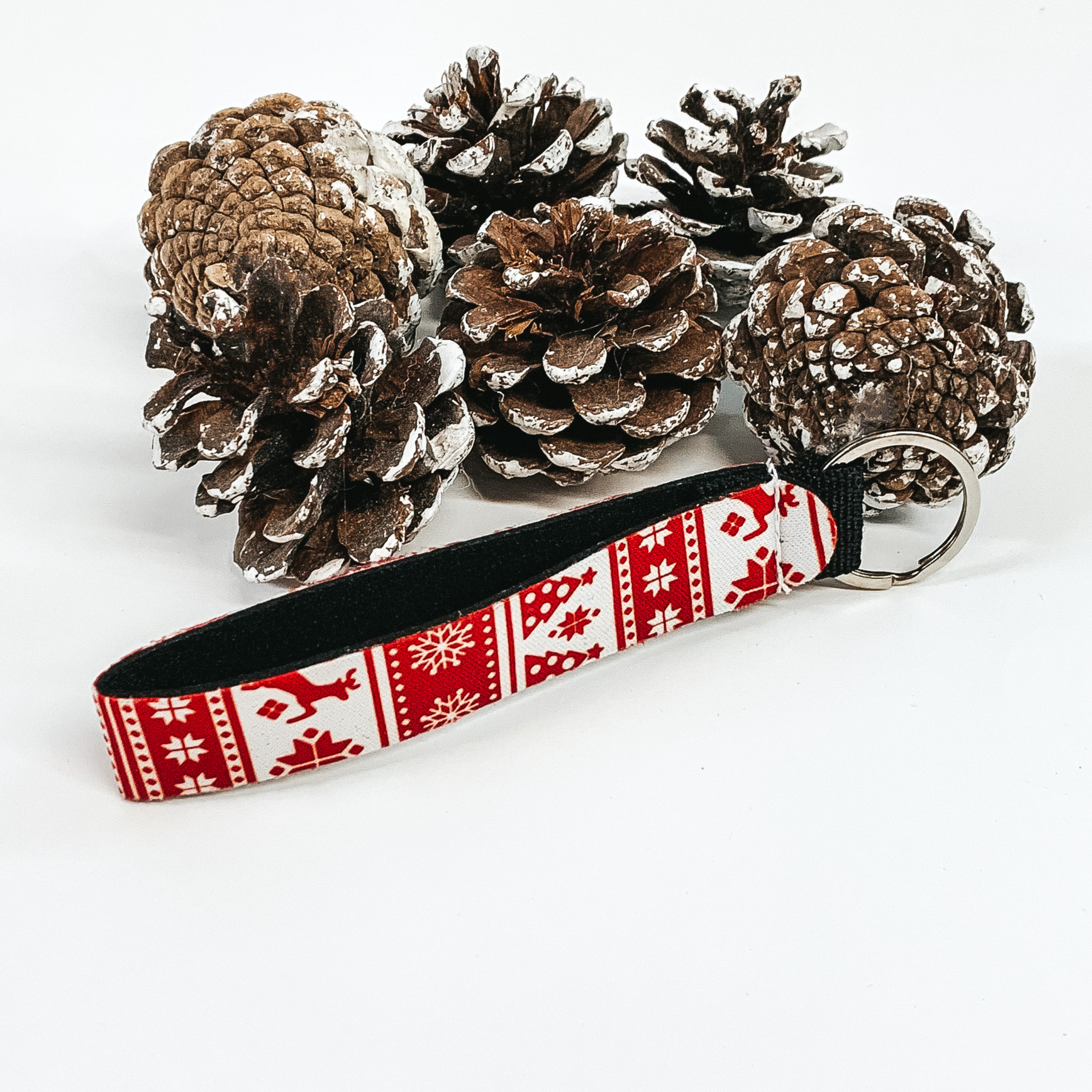 White key chain with red christmas print on a white background with pine cones