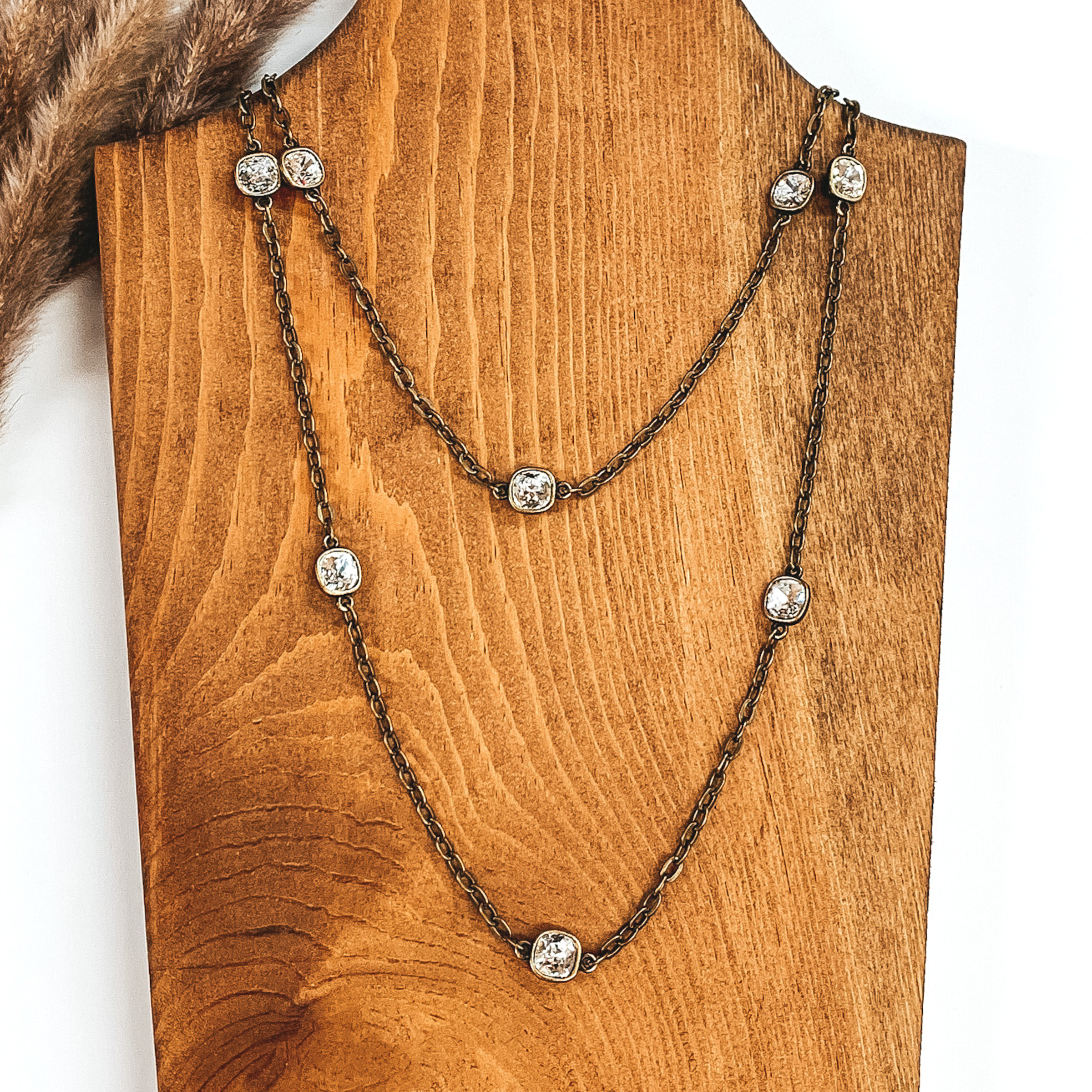 Bronze chain necklace with square clear crystal spaces pictured on a white and wood background. 