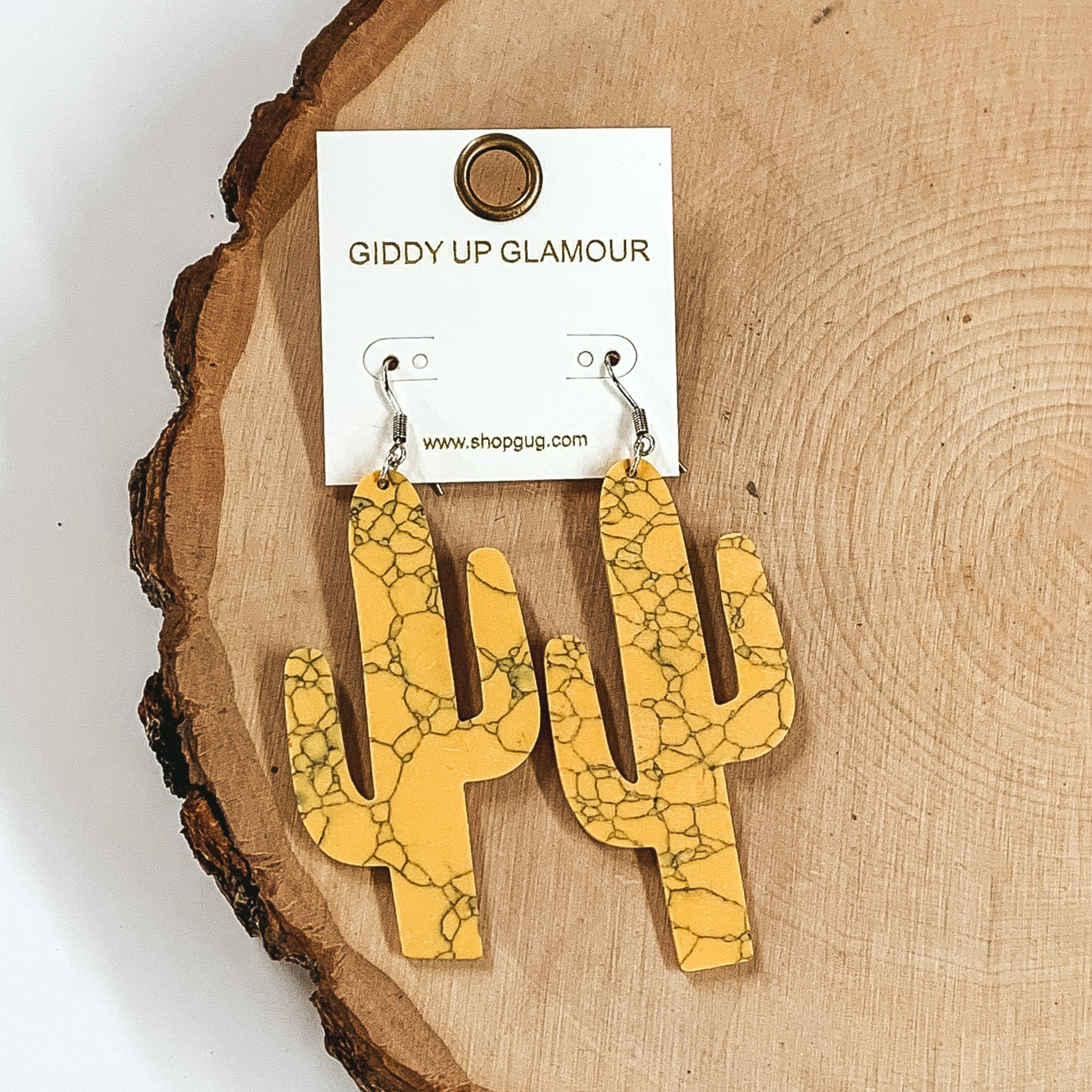 Yellow marbled cactus cutout earrings pictured on a wood background.
