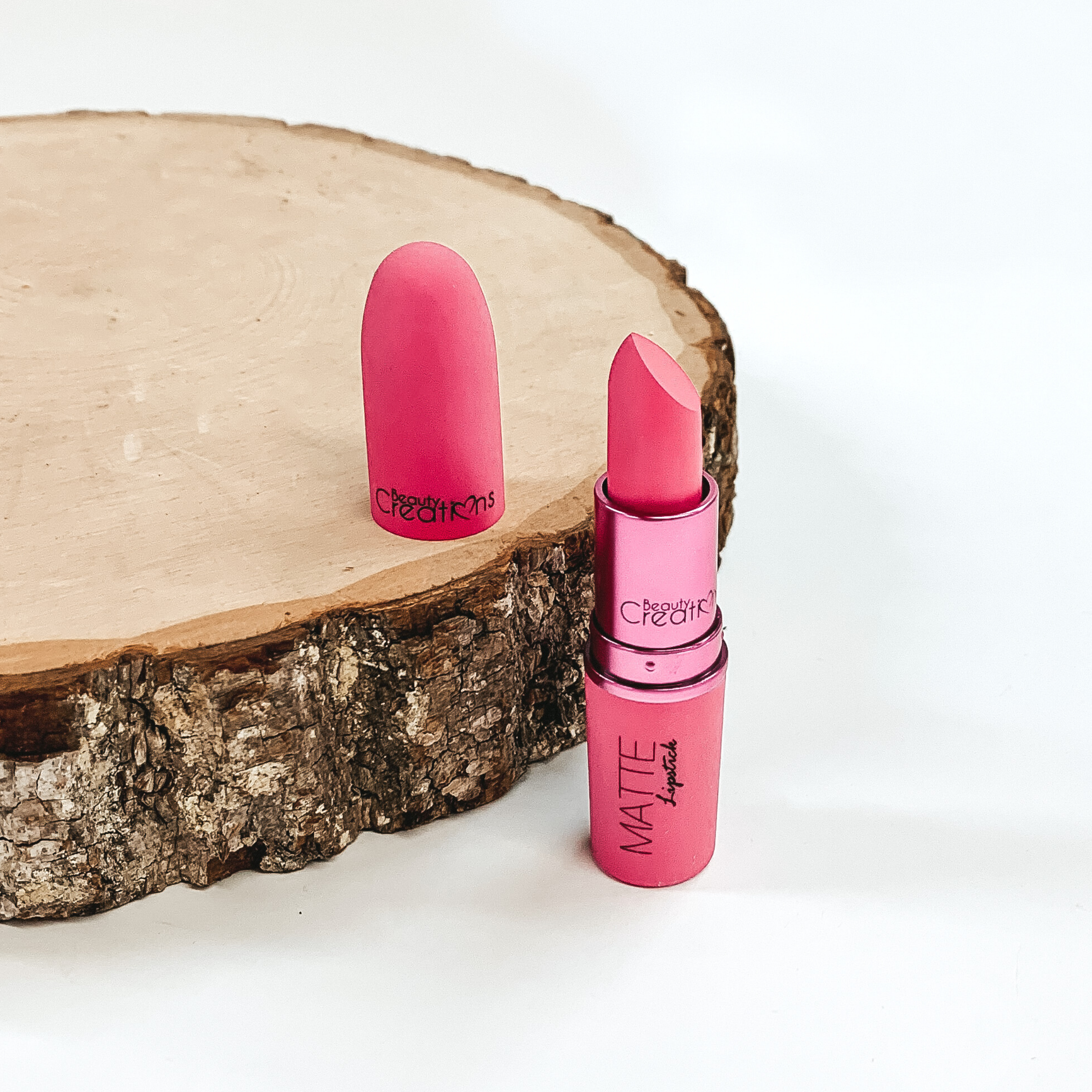 Shade pinky promise lipstick that is opened and twisted up. The tube is standing on a white background and next to it is some wood that the lid from the lipstick is placed on.