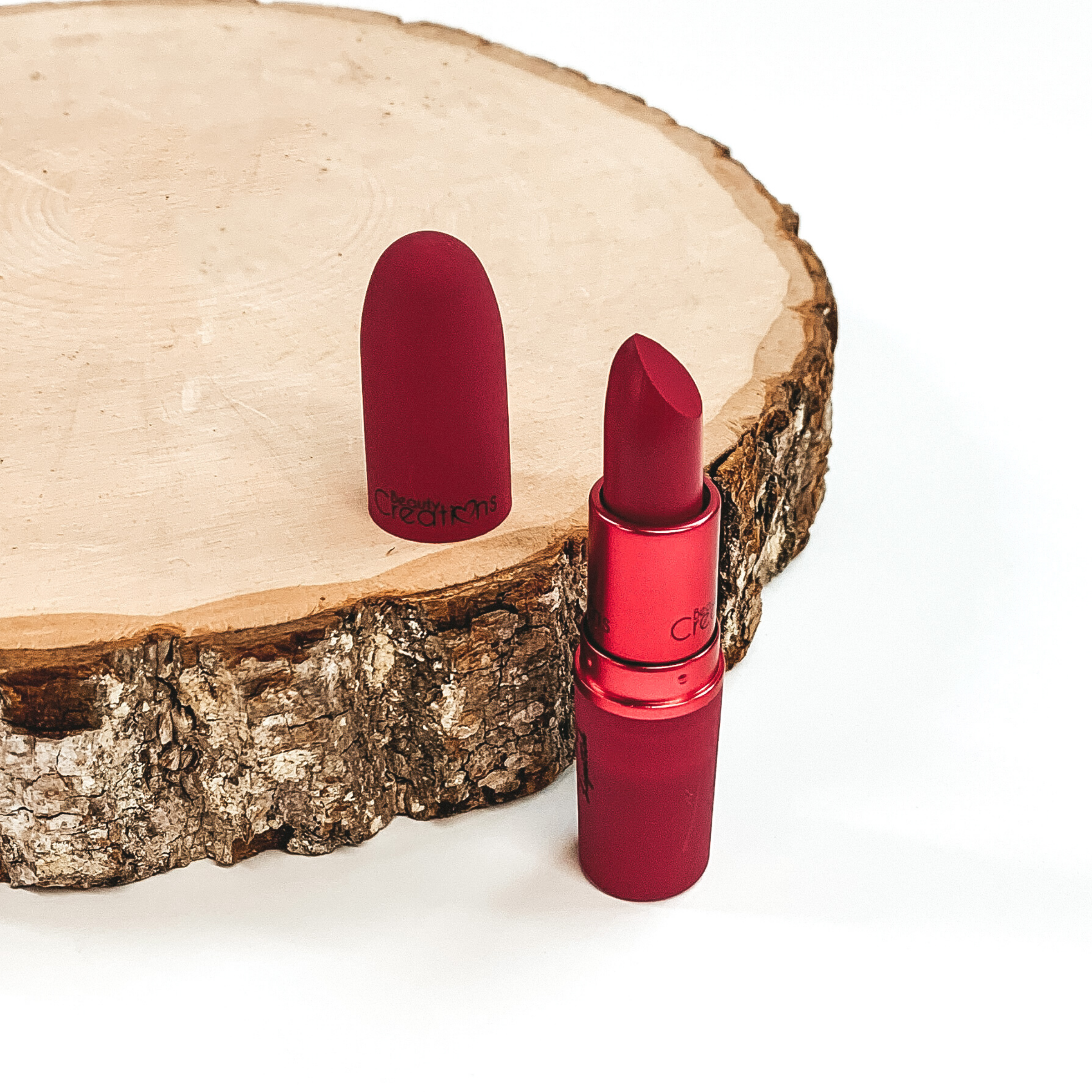 Shade sugar bomb lipstick that is opened and twisted up. The tube is standing on a white background and next to it is some wood that the lid from the lipstick is placed on.