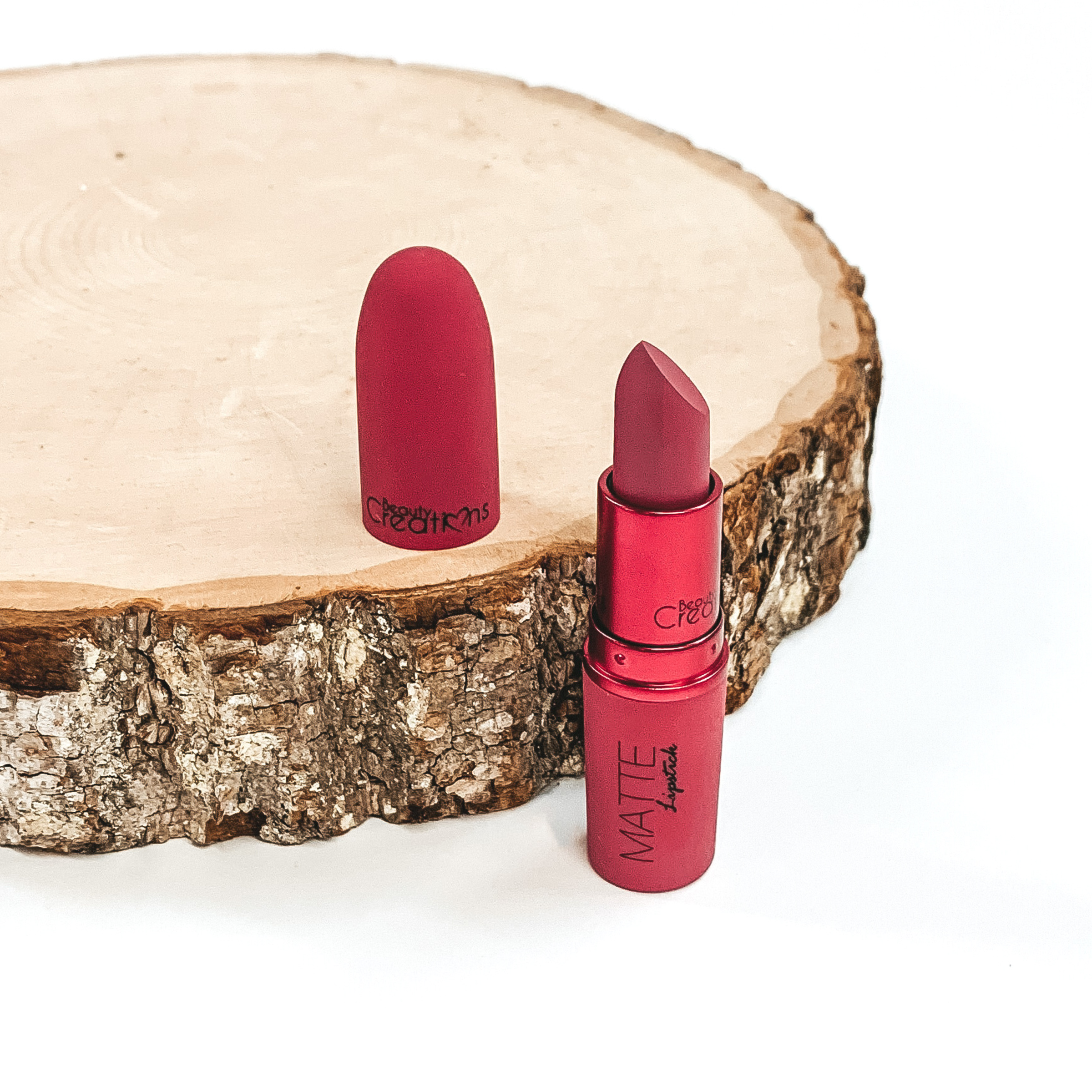 Shade bite me lipstick that is opened and twisted up. The tube is standing on a white background and next to it is some wood that the lid from the lipstick is placed on.