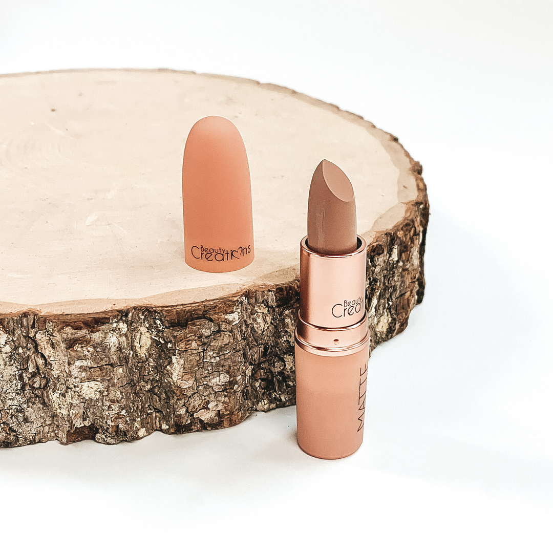 Shade sweetheart lipstick that is opened and twisted up. The tube is standing on a white background and next to it is some wood that the lid from the lipstick is placed on.