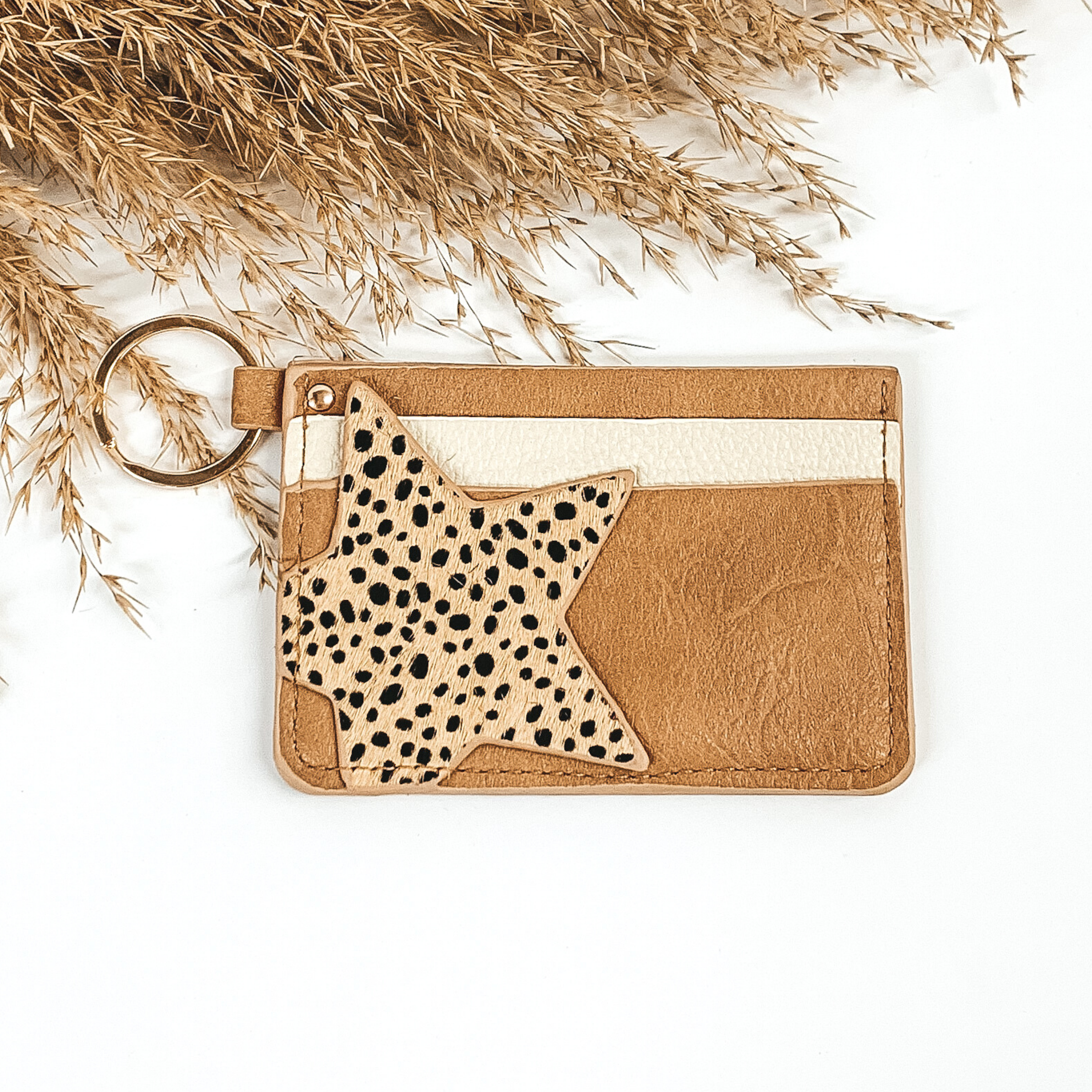 This is a rectangle id key holder that has a gold key ring. On the front you have brown and ivory layer and then a black dotted star is also on the front. It is pictured on a a white background that has brown floral at the top of the picture. 
