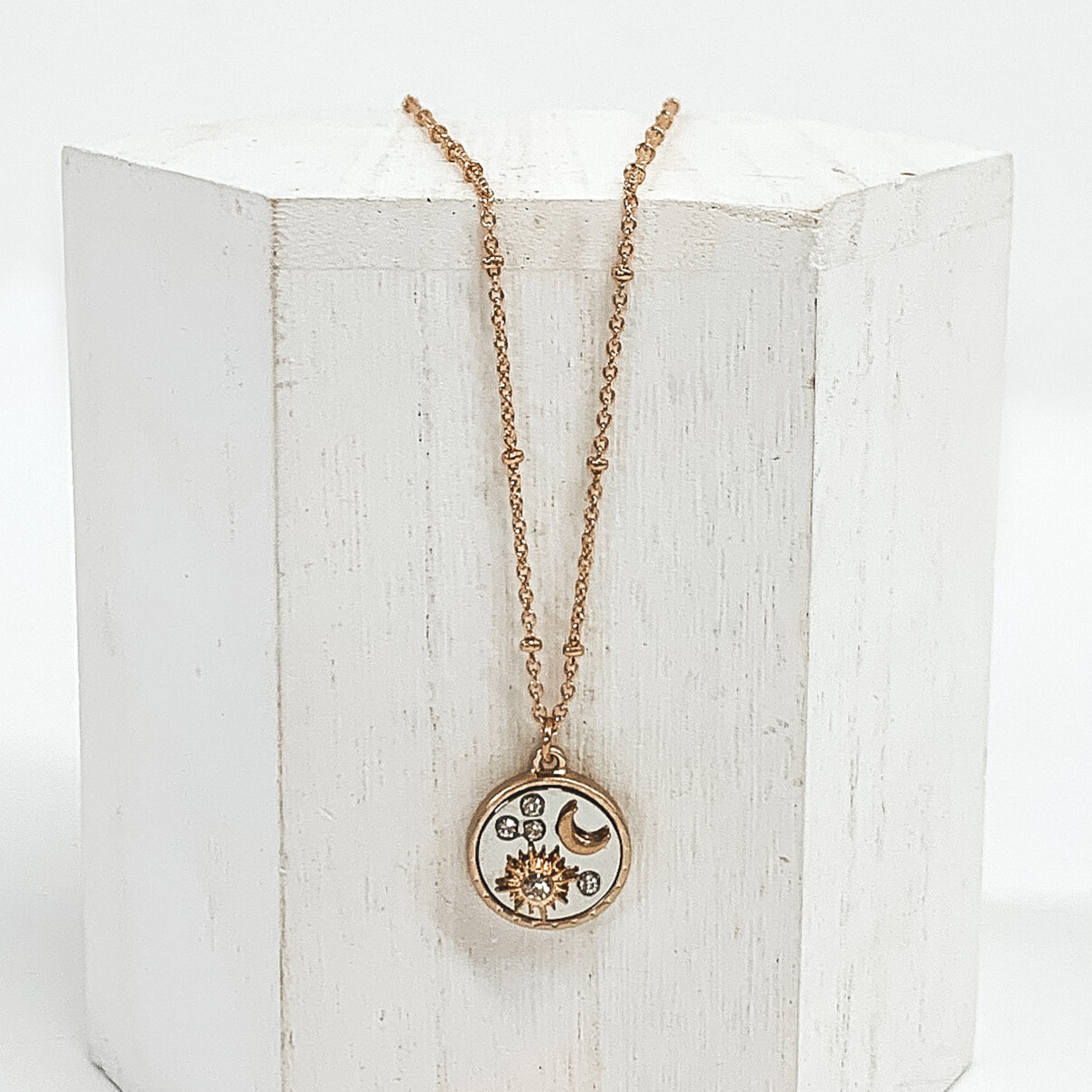 Gold necklace with gold circle pendant with a silver inlay. The circle pendant has clear round circles, a gold star, and a gold moon. This necklace is pictured on a white block and on a white background.
