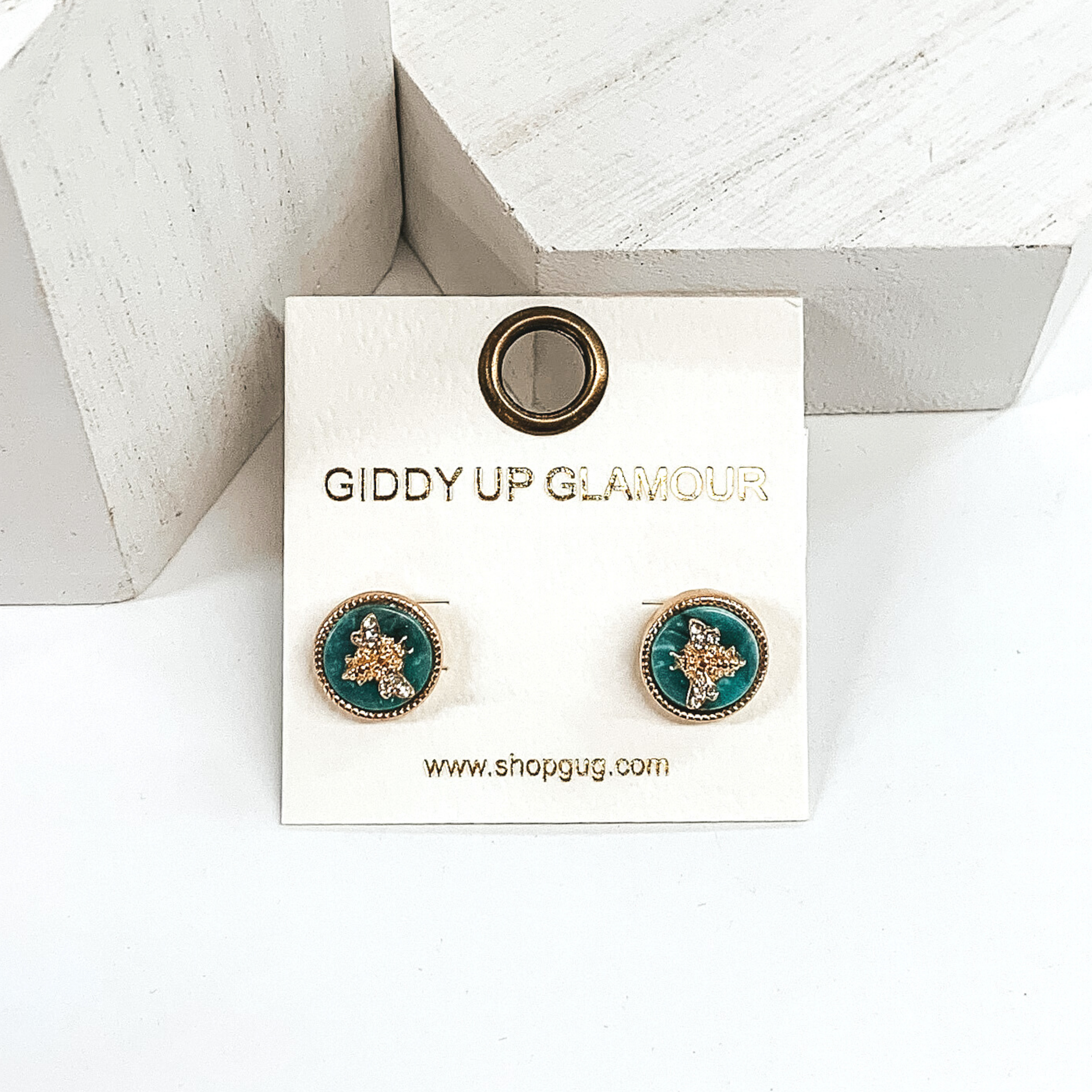 Sea green circle stud earrings with a gold bee charm in the center. There are crystals on the wings of the bee charm. These studs are pictured of a white background.