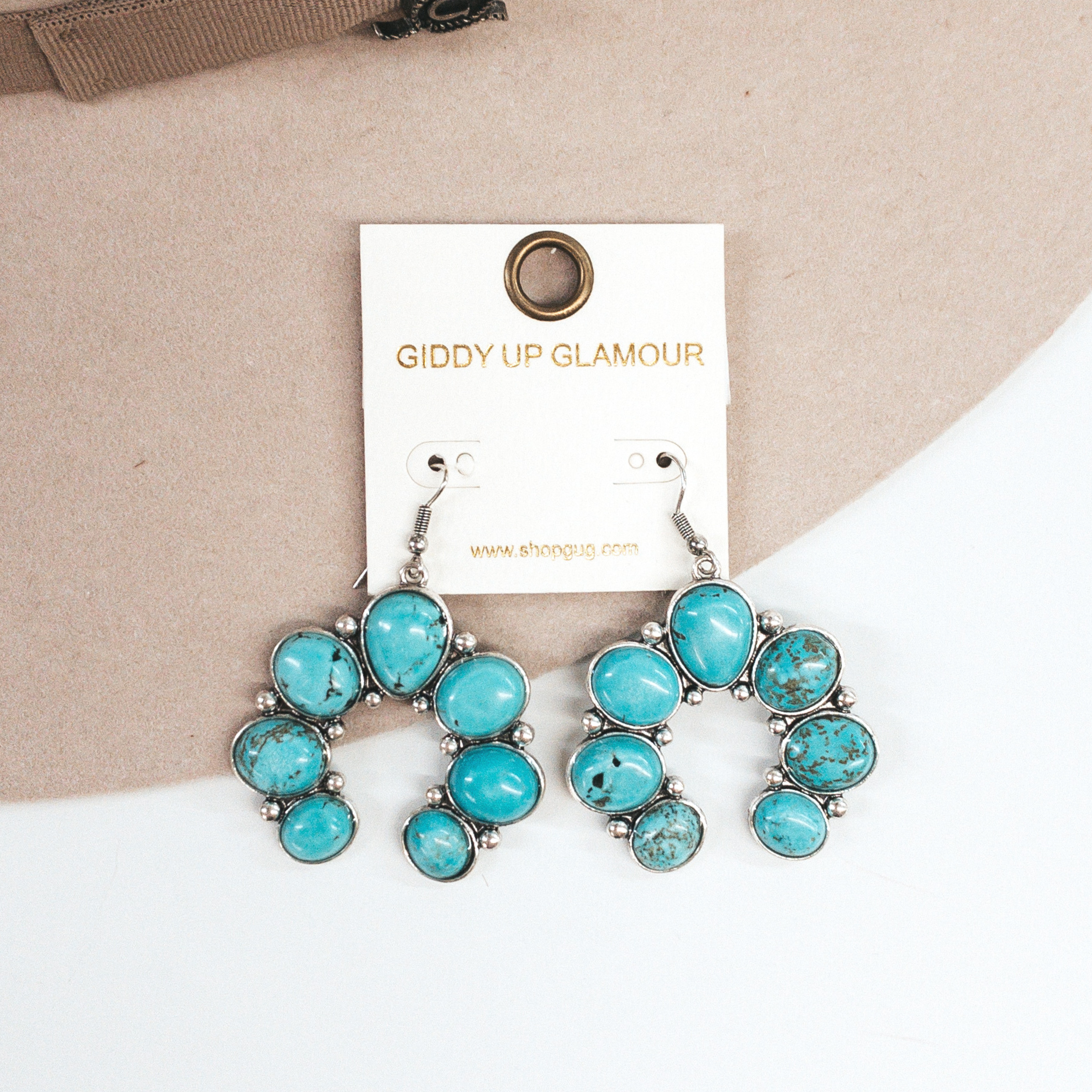 Turquoise stone squash blossom dangle earrings with a silver backing. Pictured on a a white and beige background. 