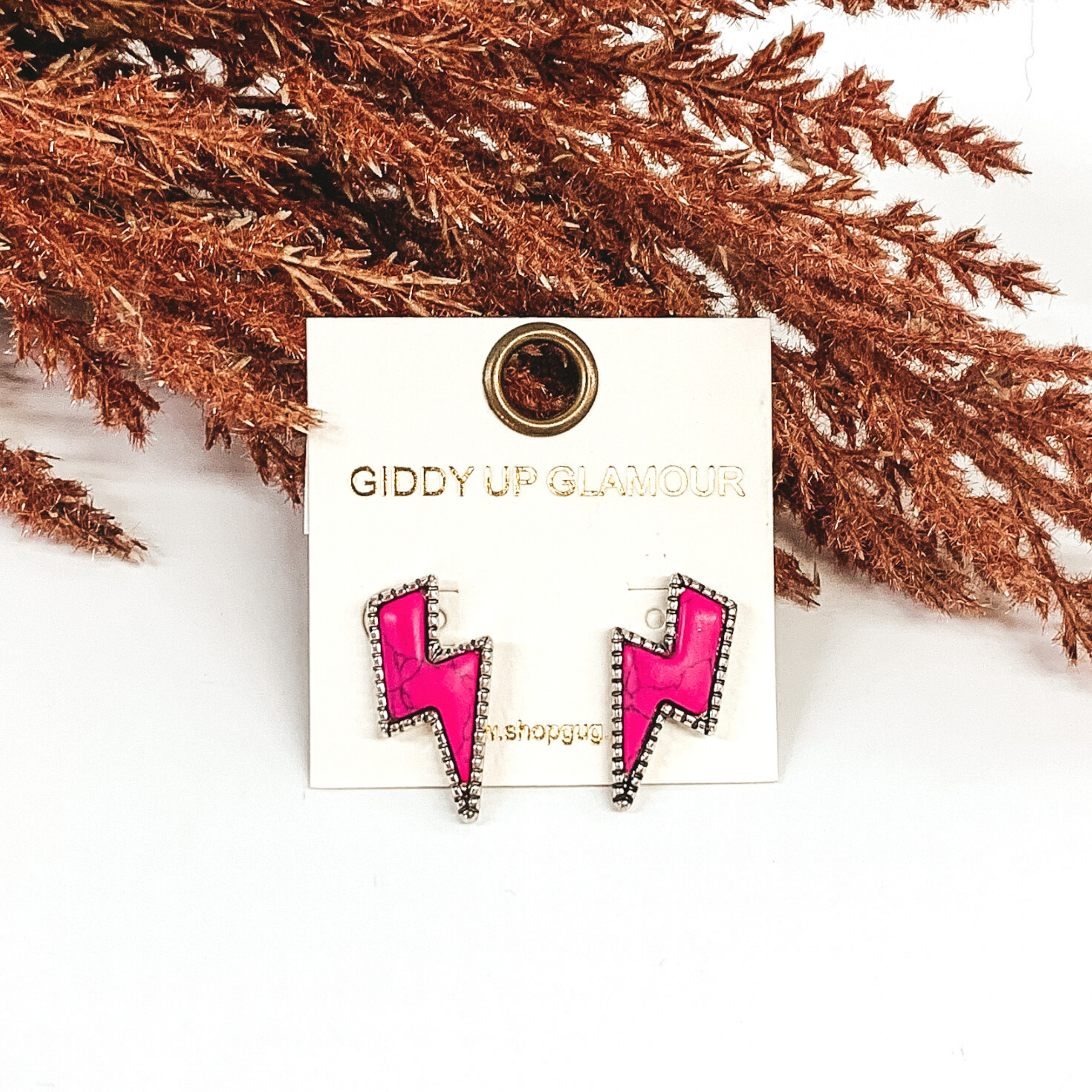 Pink stone stud earrings in a lightning bolt shape with a silver backing. They are pictured on a white background with brown floral decor. 