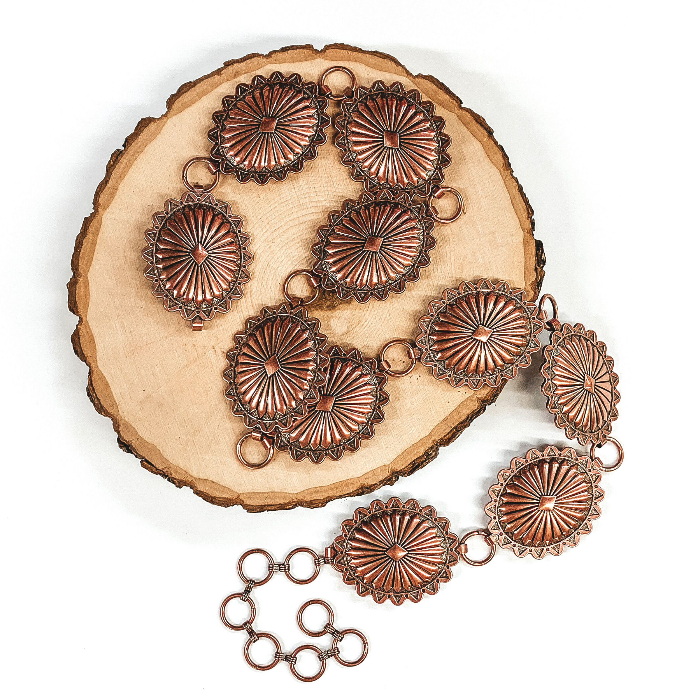 Copper concho belt laid on a piece of wood that is pictured on a white background. 