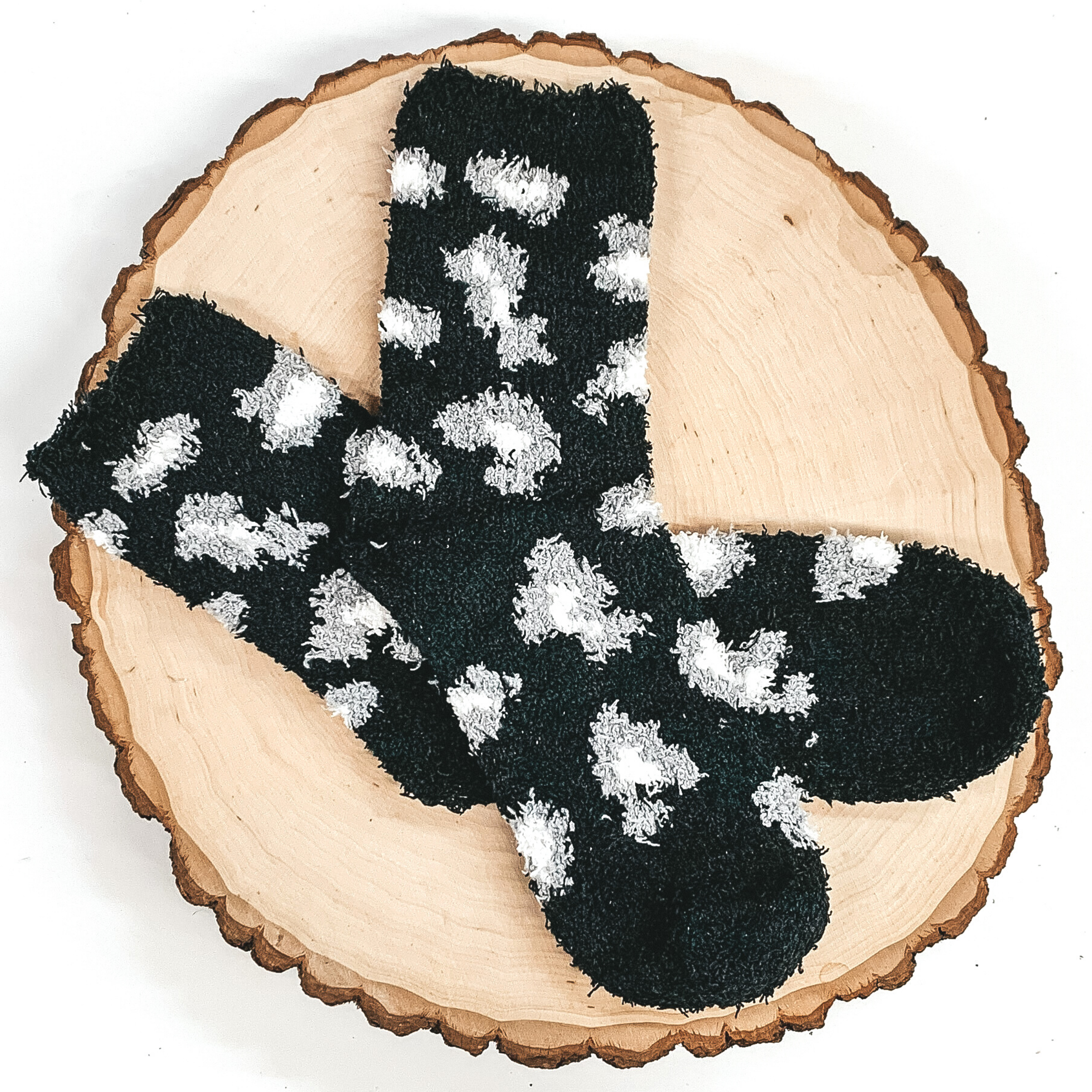 Fuzzy black socks with white and grey leopard print. These socks are pictured laying on a piece of wood that is on a white background.