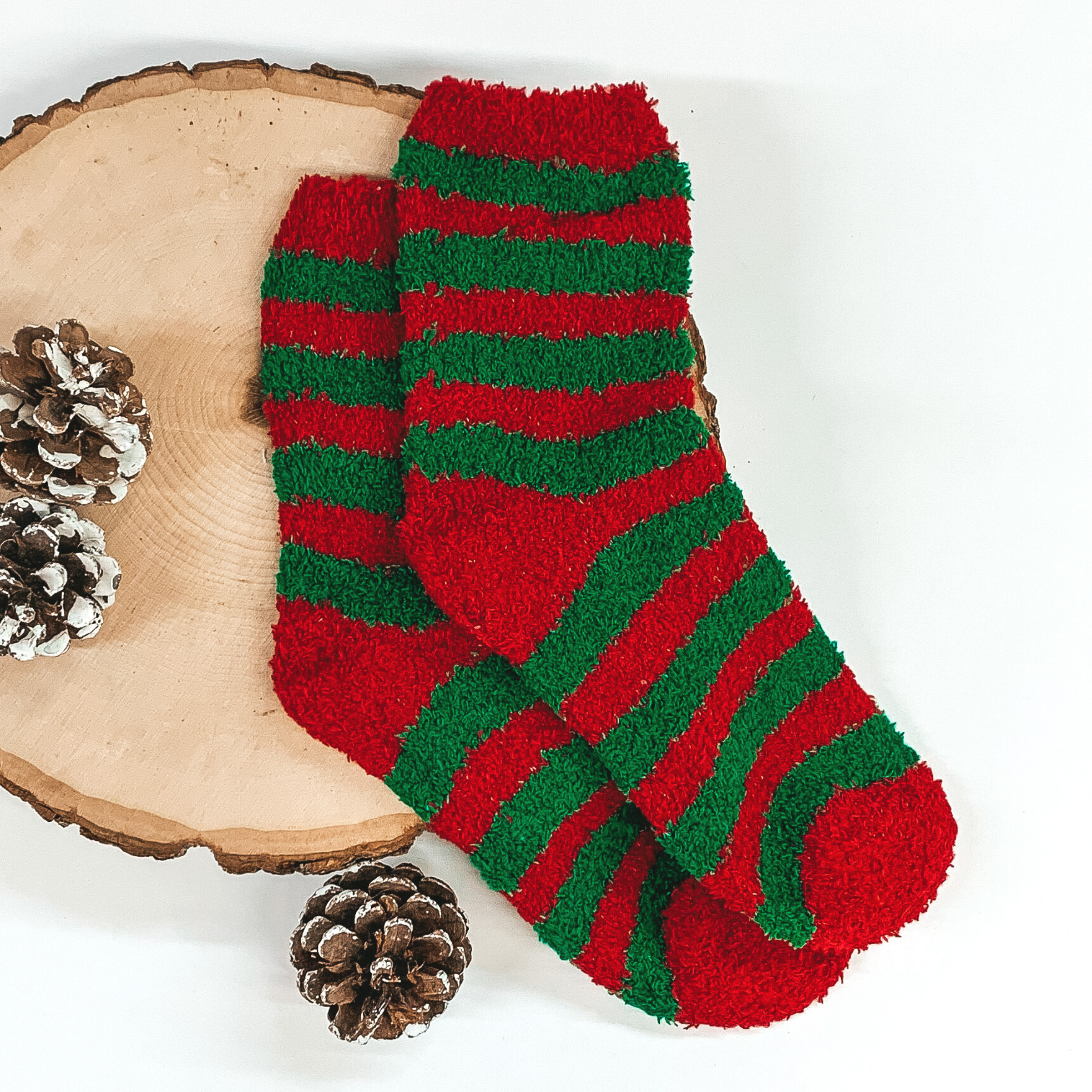 Fuzzy red and green striped socks. These socks are pictured laying on a piece of wood that is on a white background.