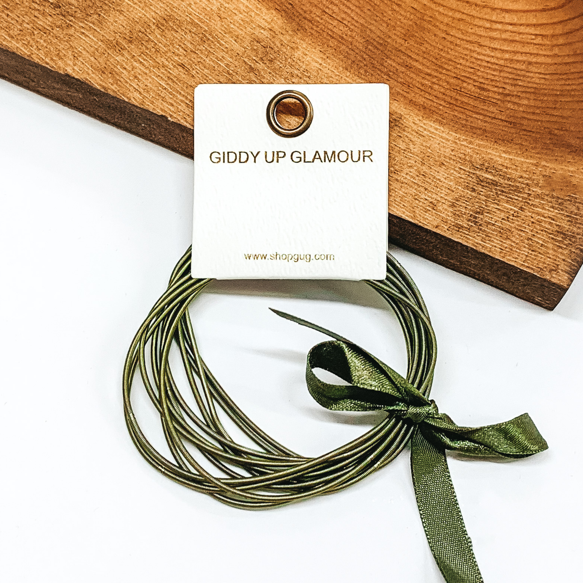 Group of olive green spring wire elastic bracelet set tied together with an olive green ribbon that is tied in a bow. This bracelet set is pictured laying against a piece of wood on a white background. 