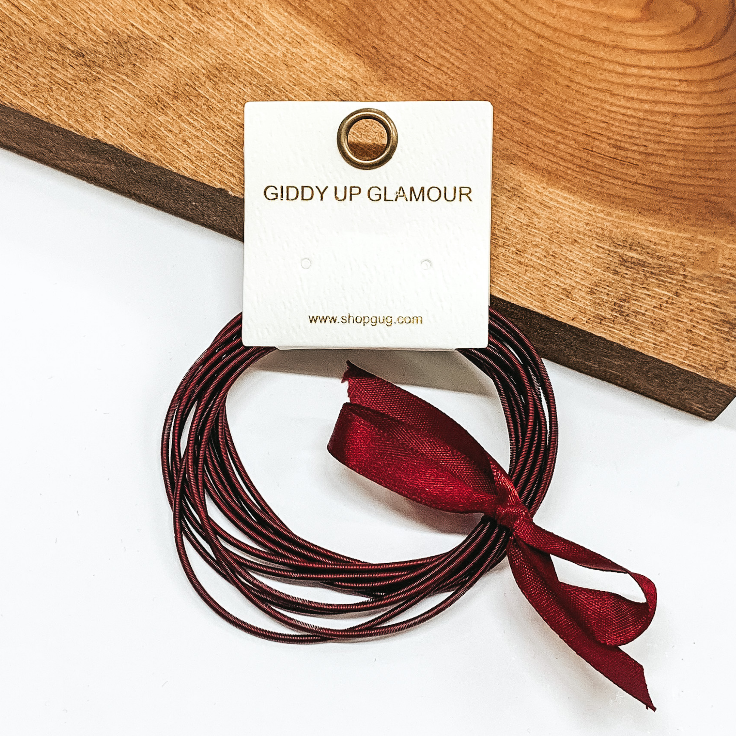Group of maroon spring wire elastic bracelet set tied together with a maroon ribbon that is tied in a bow. This bracelet set is pictured laying against a piece of wood on a white background.