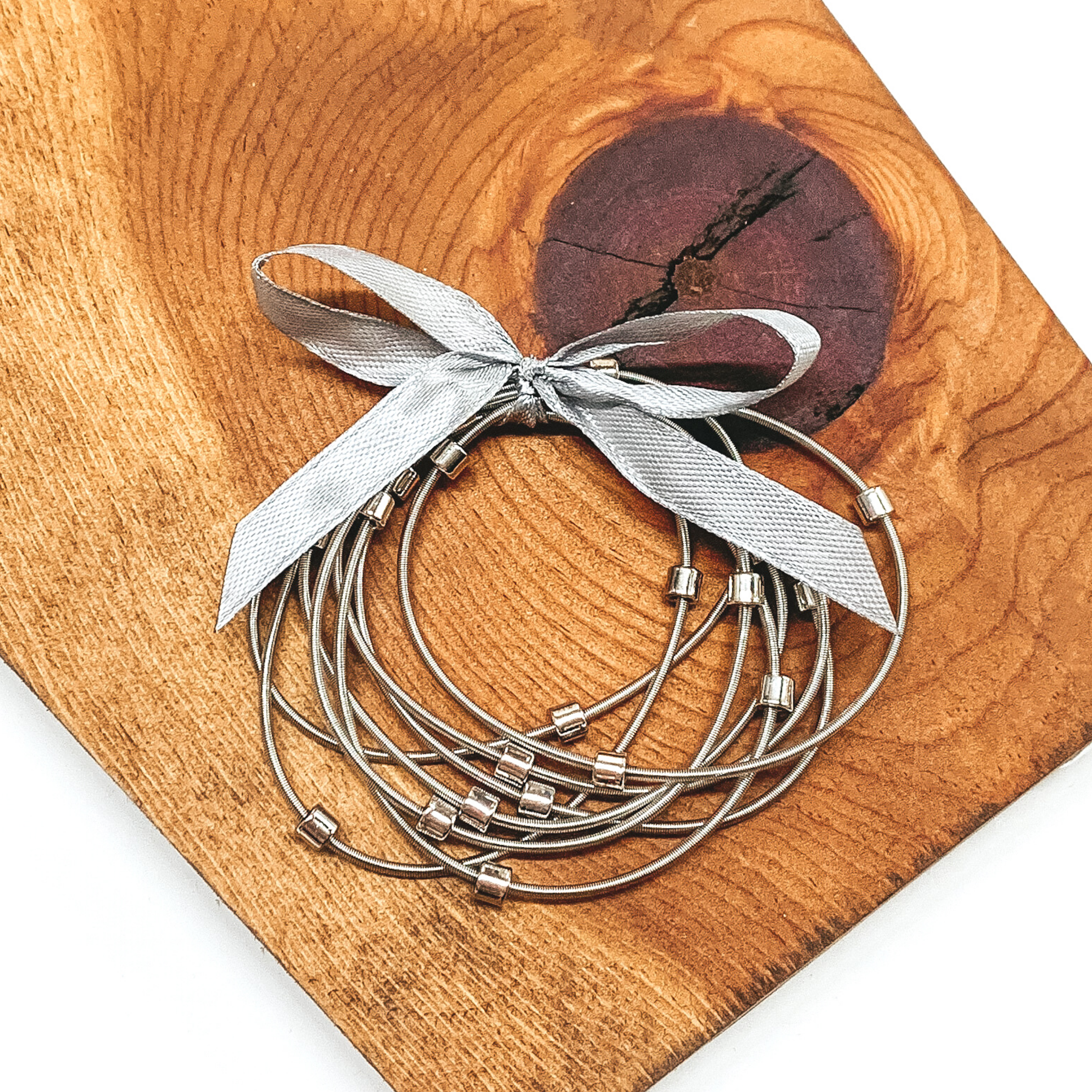 Group of silver spring wire elastic bracelet set tied together with a silver ribbon that is tied in a bow. All of the bracelets have small silver beads. This bracelet set is pictured laying next on a piece of wood on a white background.