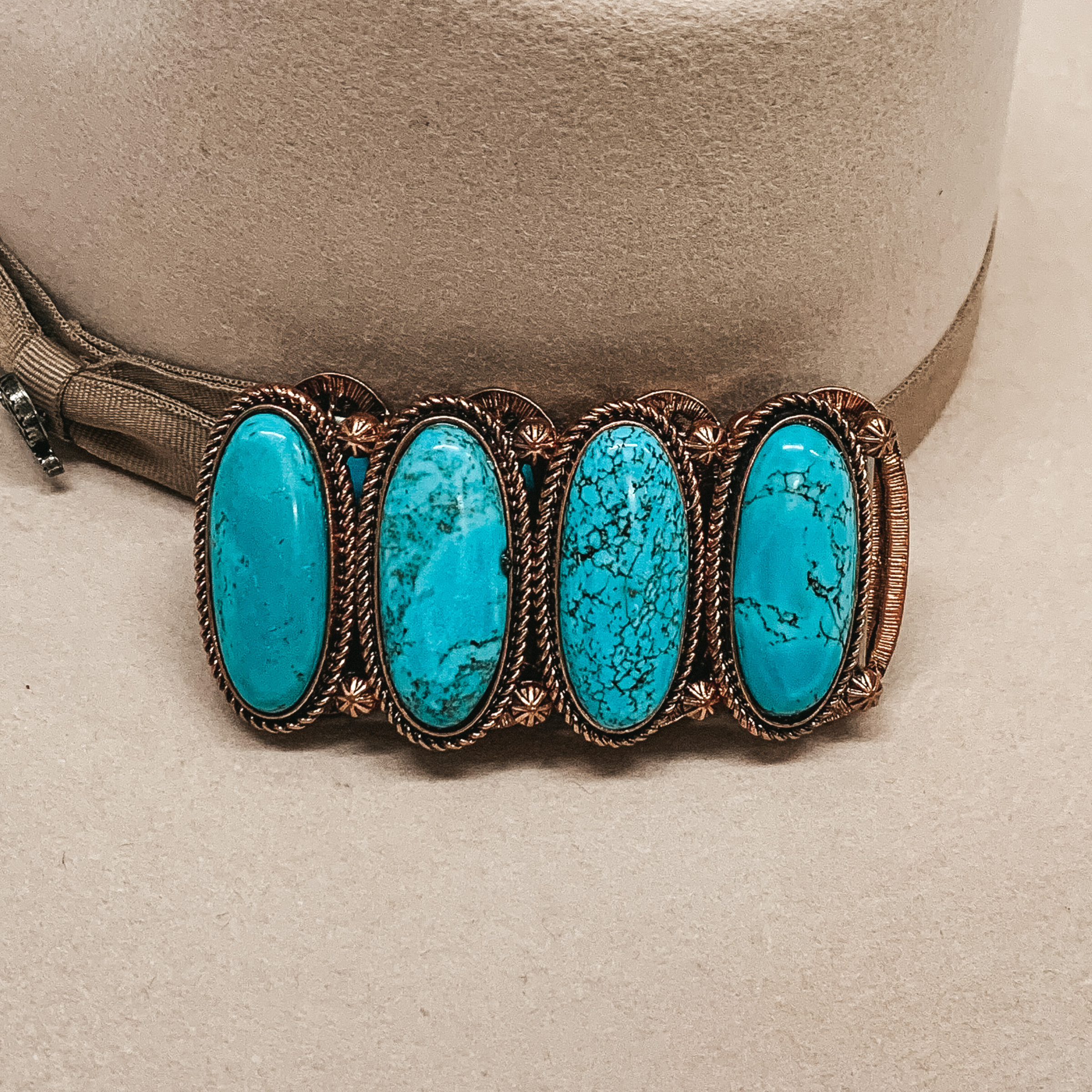 Copper bracelet with big oval turquoise stones pictured laying on a beige background. 