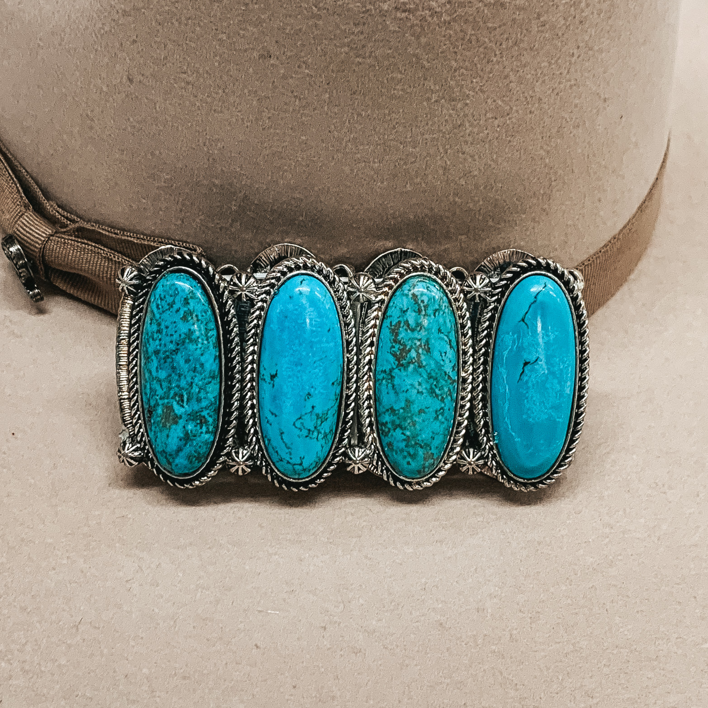 Silver bracelet with big oval turquoise stones pictured laying on a beige background.